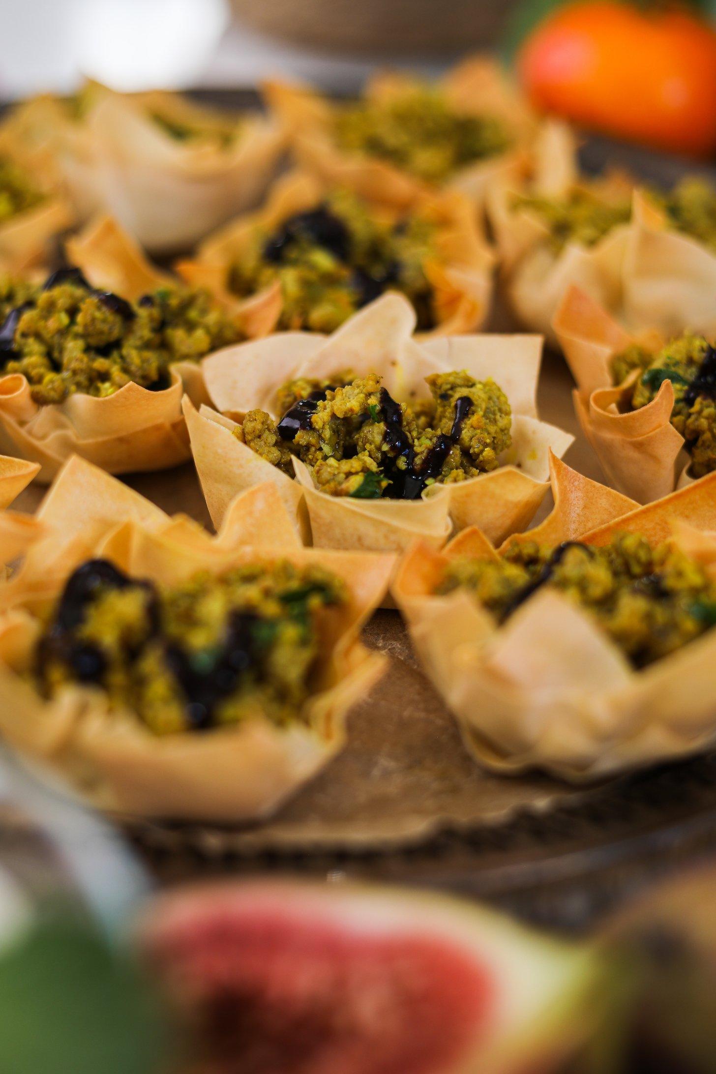 Perspective image of pastry shells filled with chicken mince and drizzled with a black chutney.