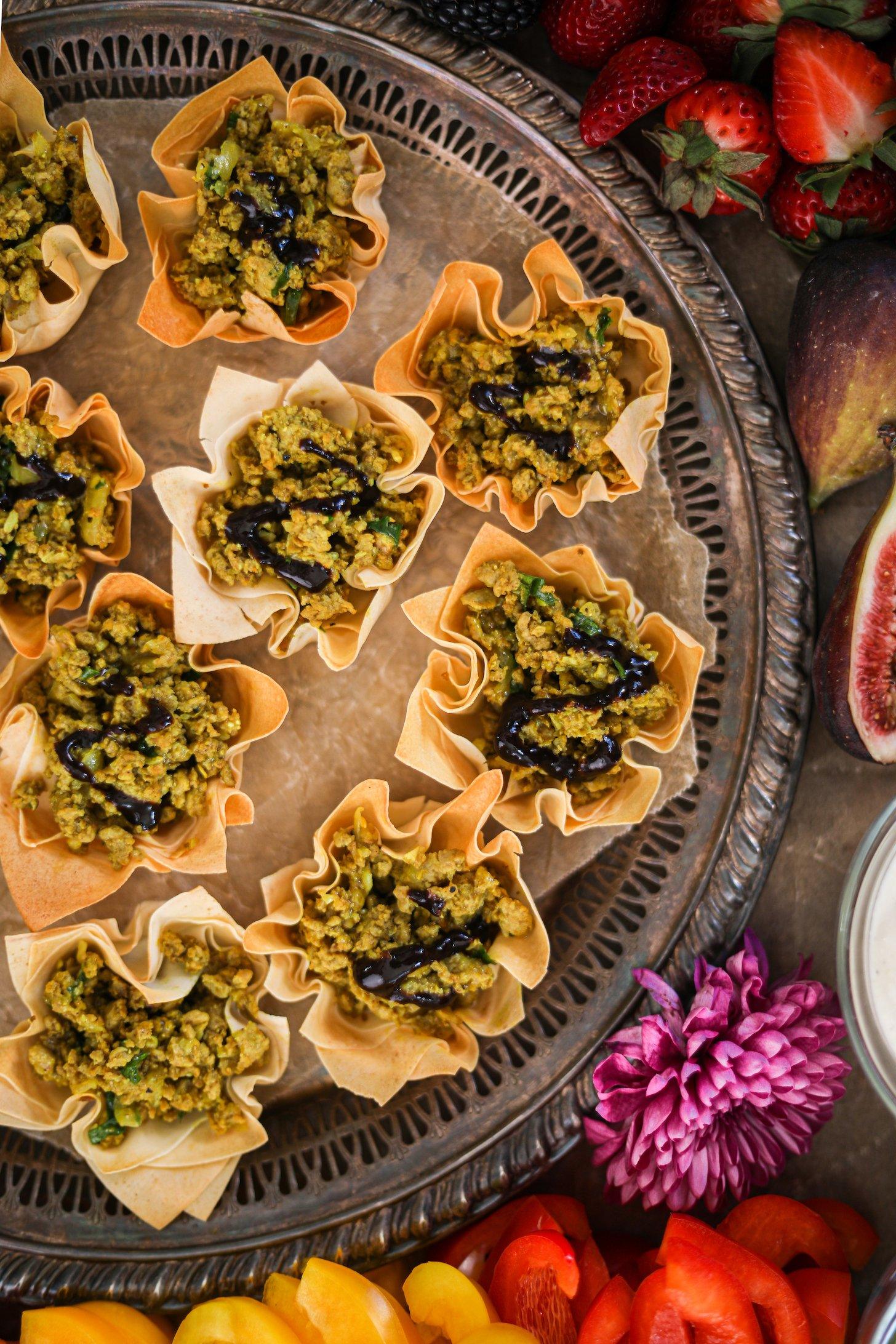 Half view of a tray of pastry shells filled with minced chicken and drizzled with a dark chutney.