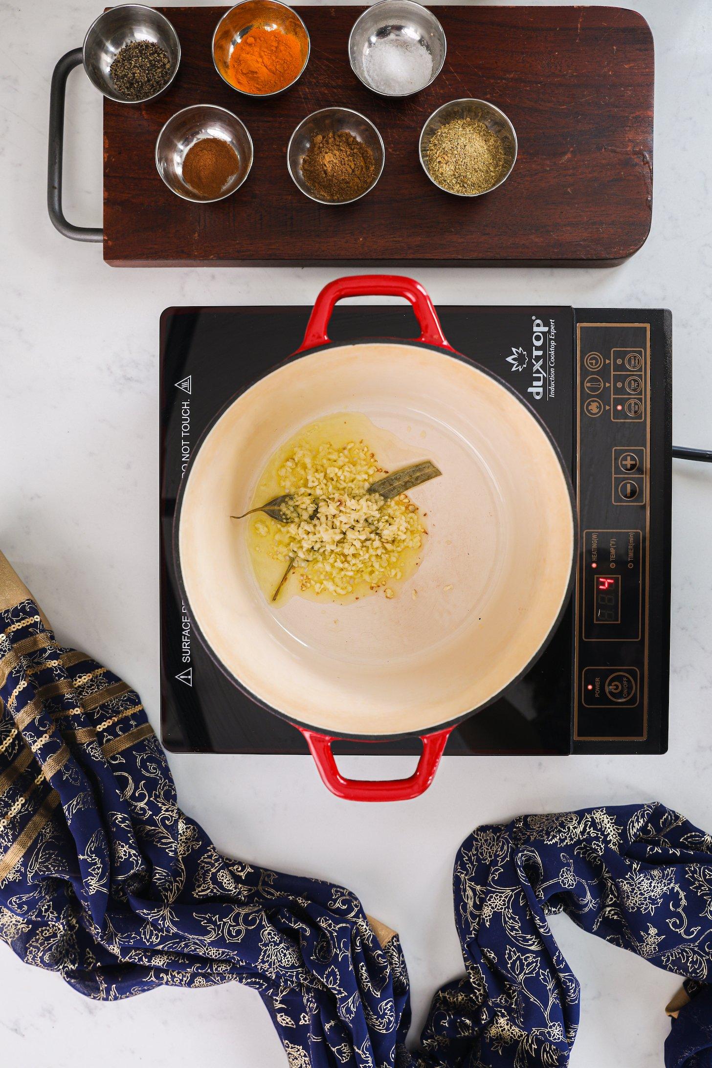 Chopped garlic and bay leaves frying in oil in a pot on a mobile cooker.