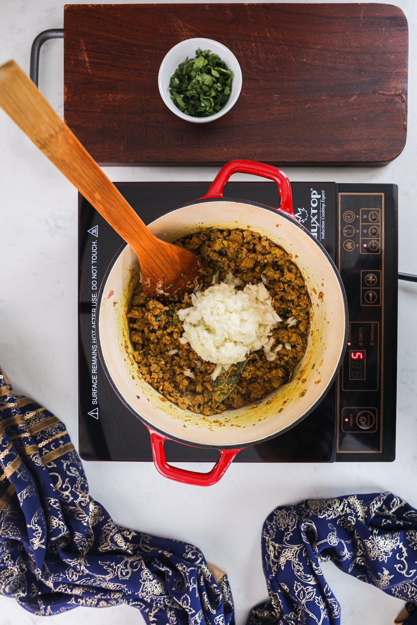 A pot of chicken topped with chopped onion on a mobile cooktop.