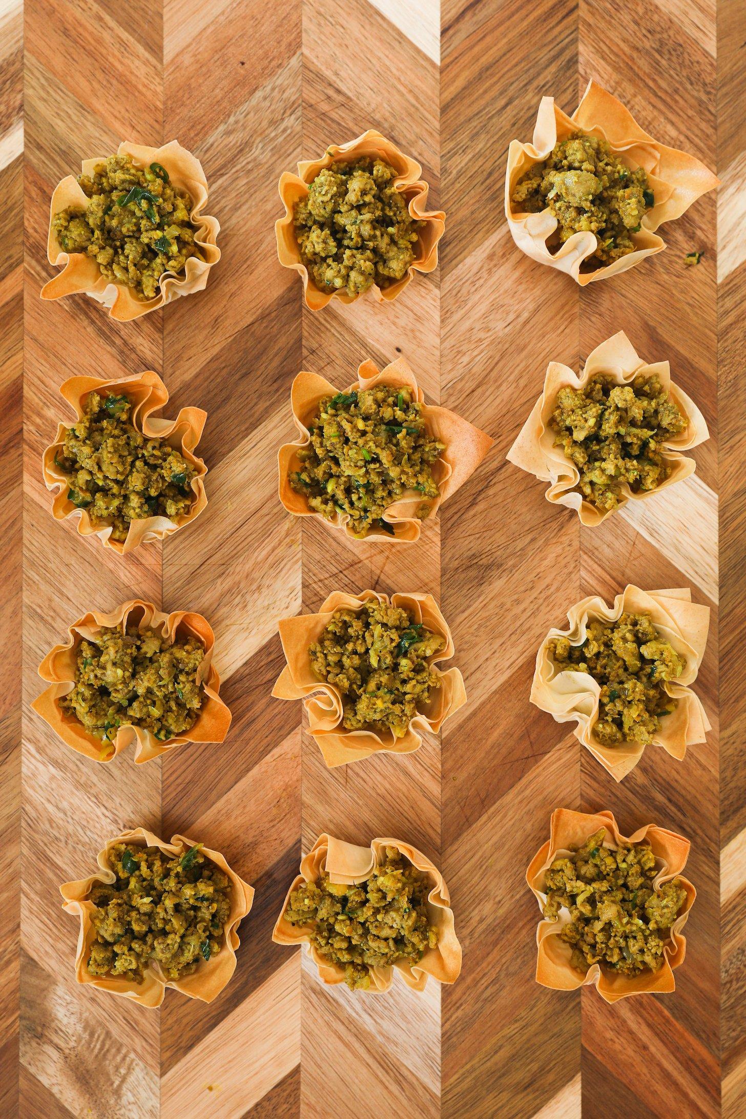 Baked flower-shaped pastry shells filled with minced chicken on a wooden board.