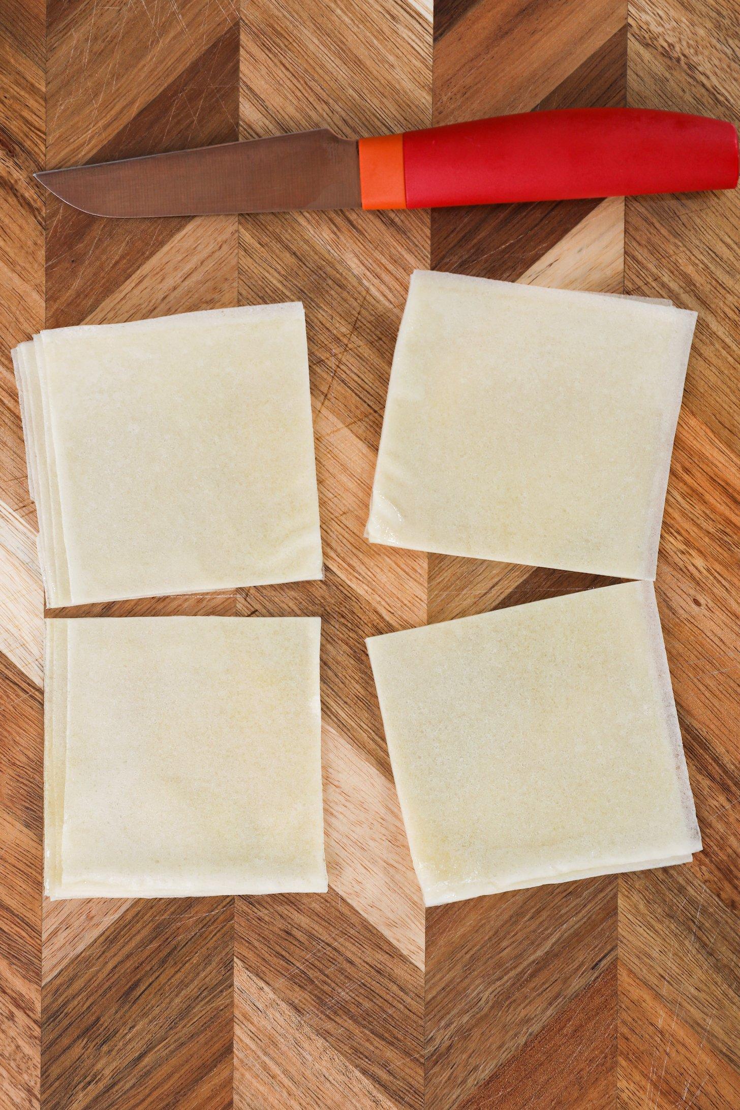 Four square stacks of spring roll pastry beside a red knife.