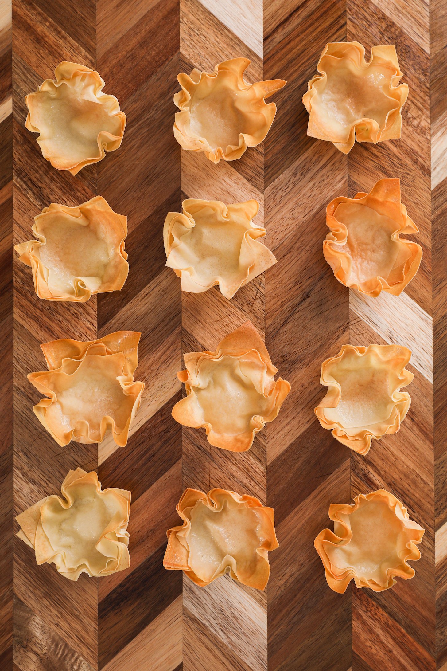 12 baked pastry shells shaped like a flower on a wooden tray.