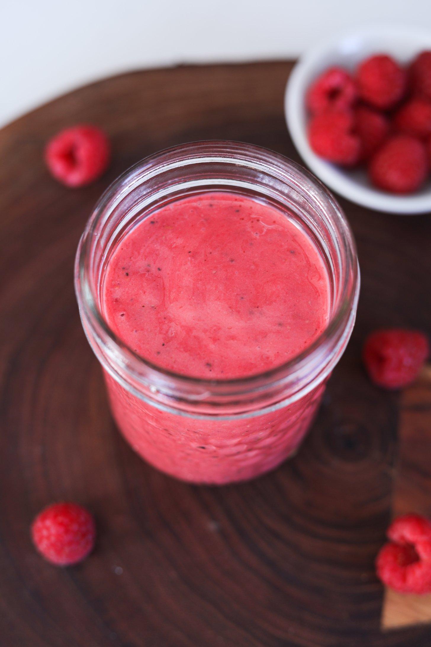 A perspective image of a red sauce surrounded by scattered raspberries.