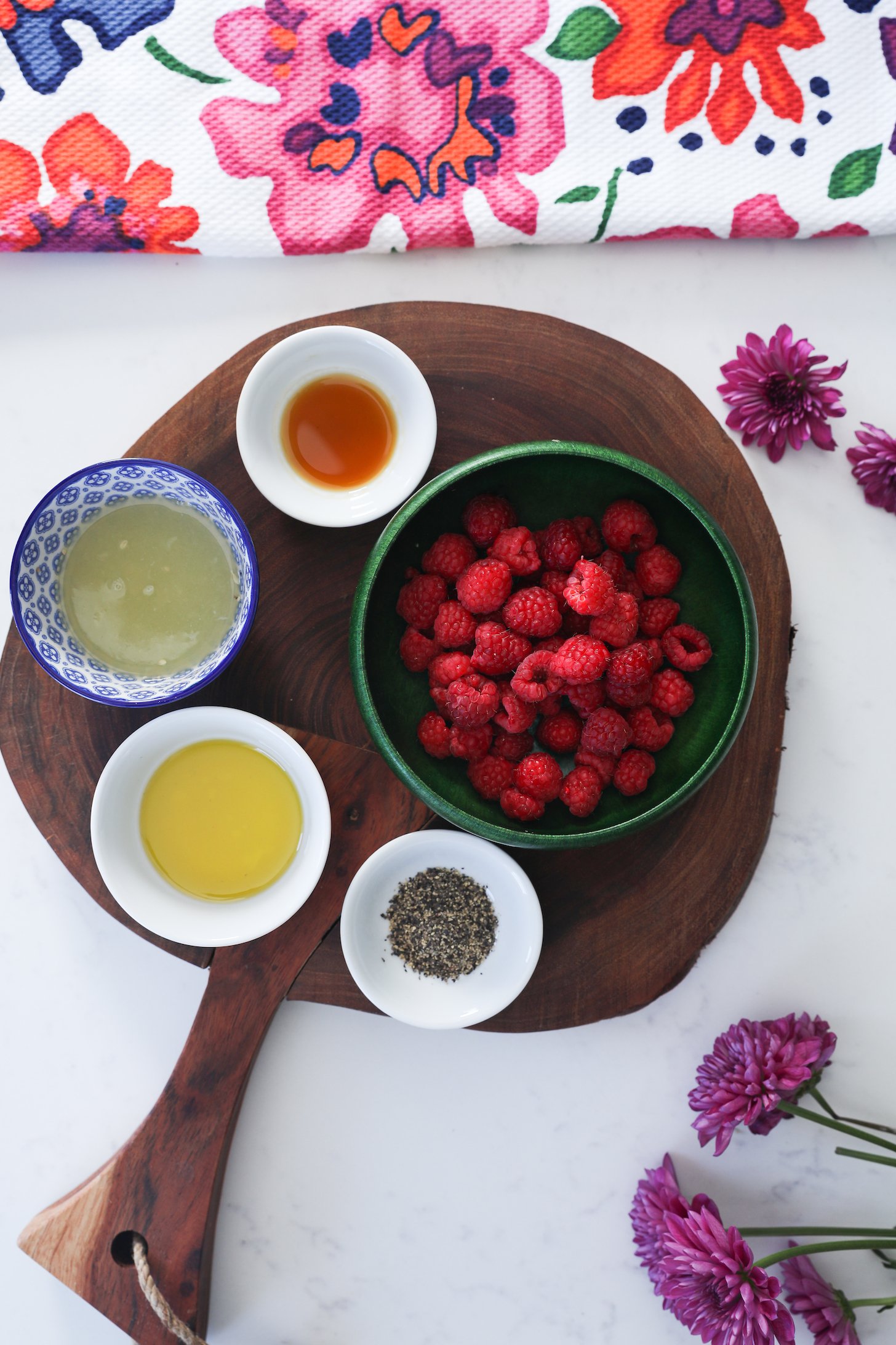 A birdseye view of food ingredients like fresh raspberries, oil, lemon and pepper on a wooden board.