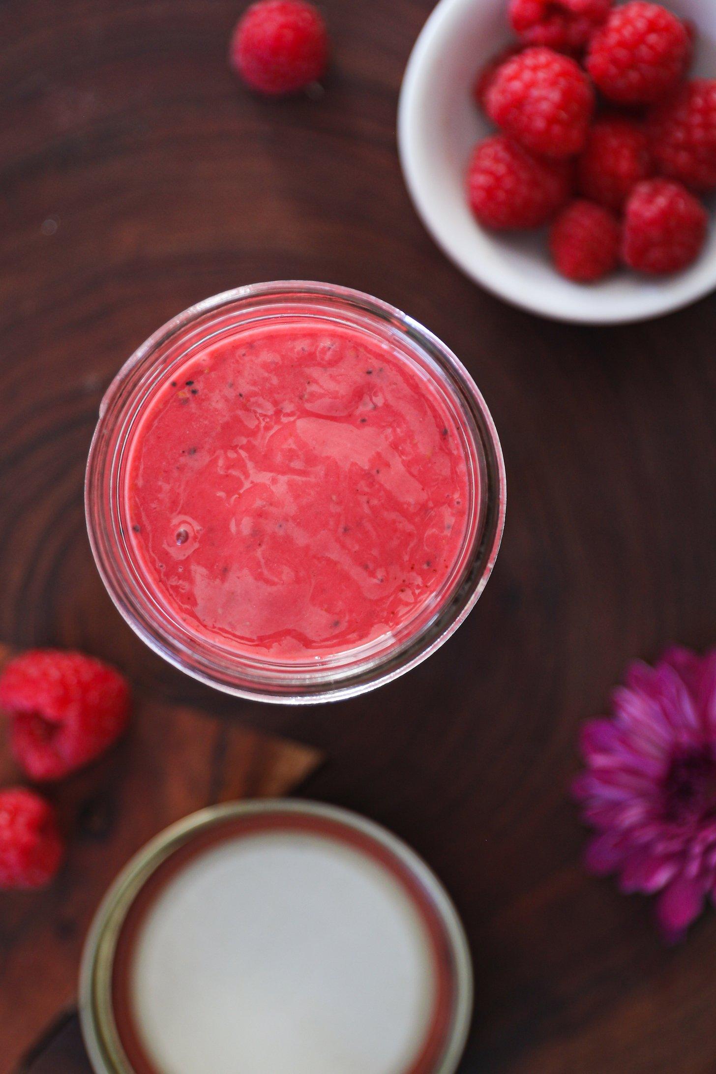 Birdseye view of a red sauce in a jar with a ramekin of raspberries nearby.