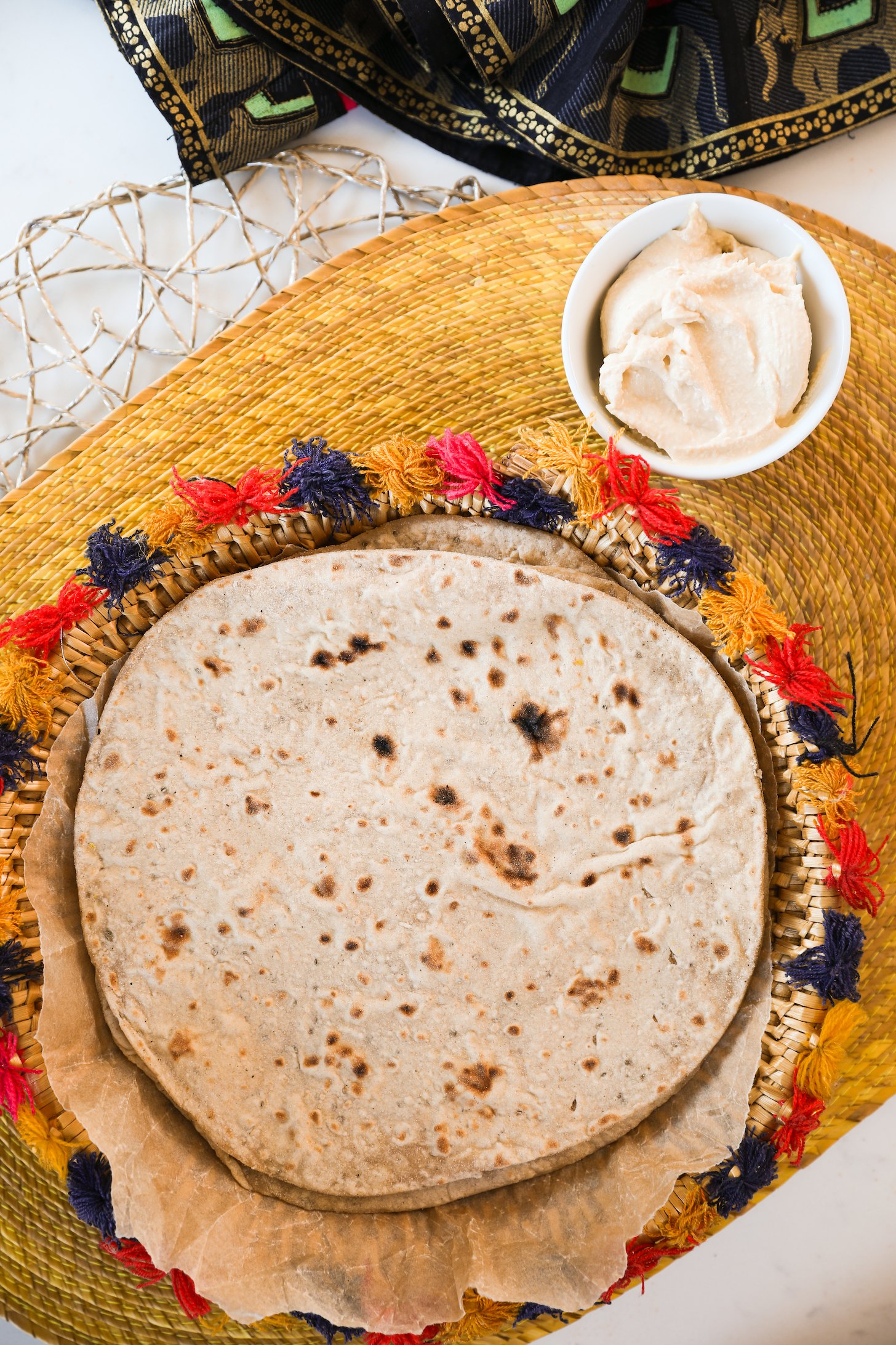 An overview of a stack of soft Rotis accompanied by a ramekin of creamy hummus.