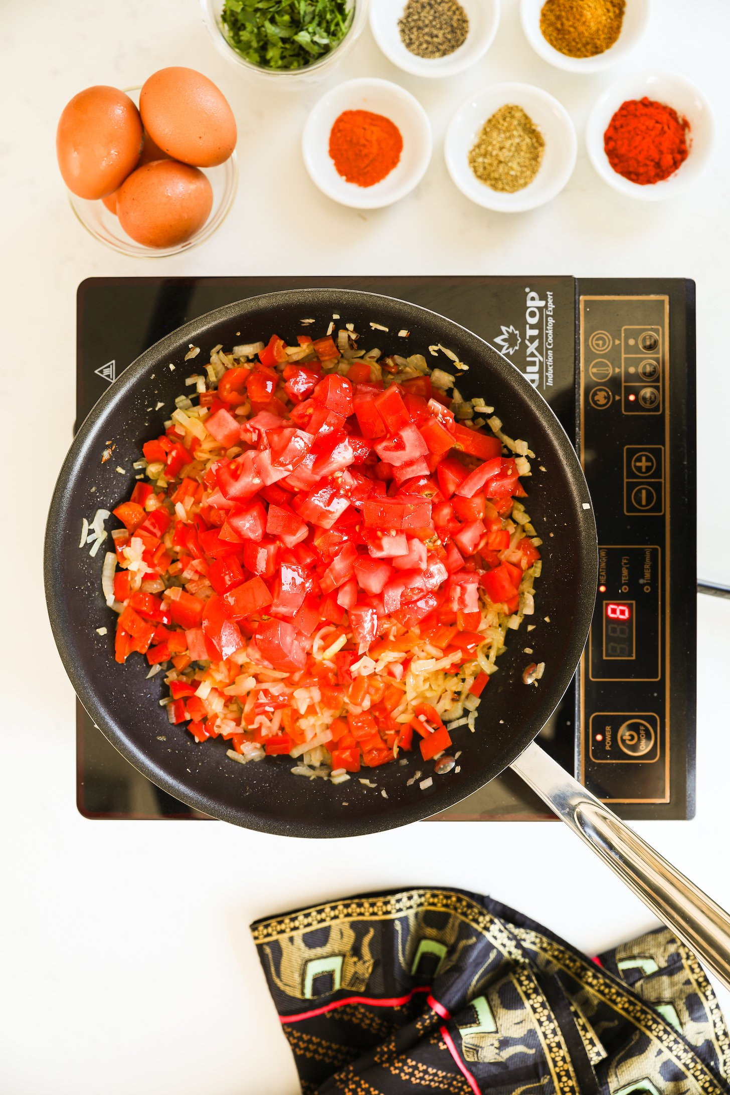 Overhead view of a pan of chopped peppers, tomatoes and onion frying in oil.