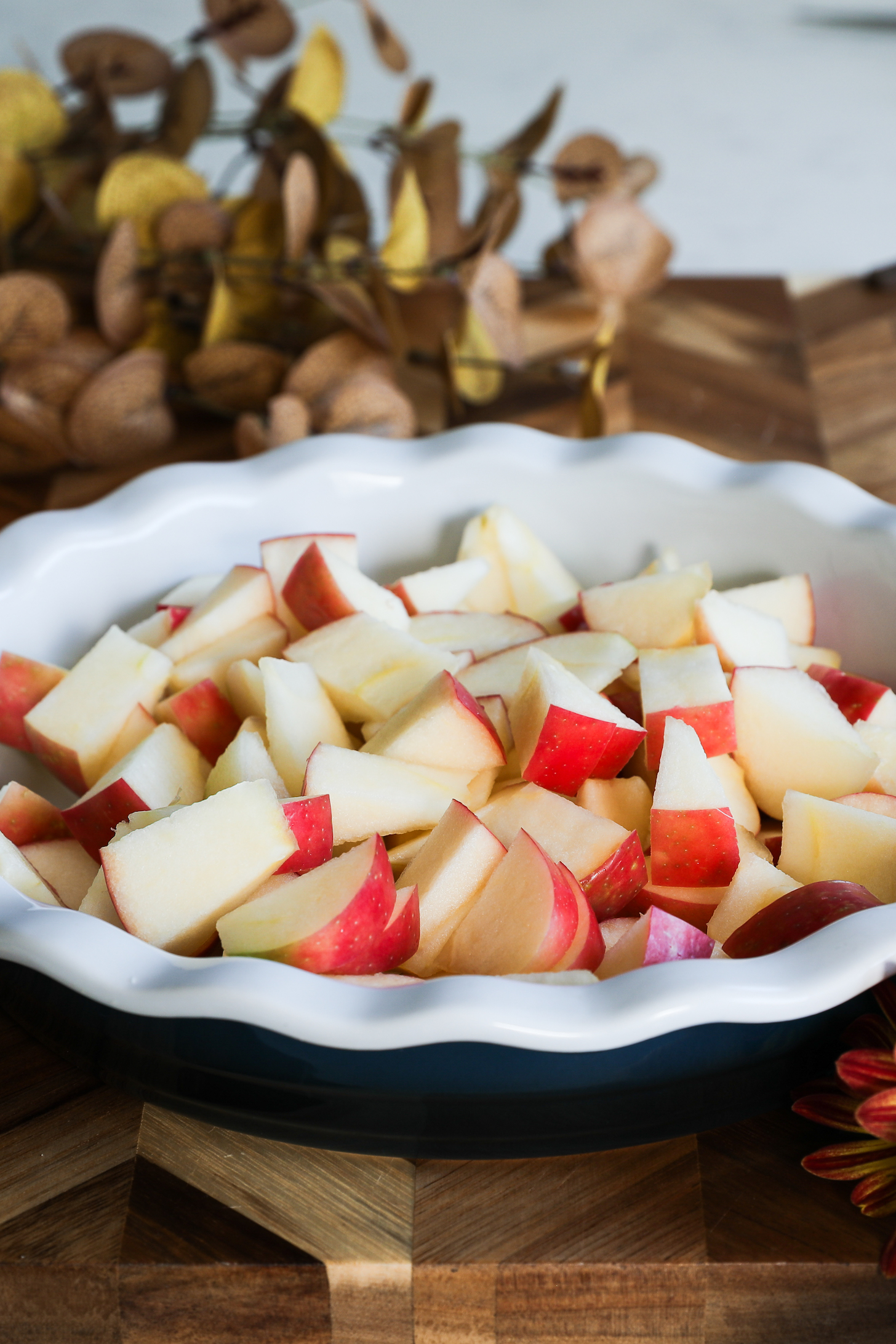 Oven dish with apple slices with flowers in the background.