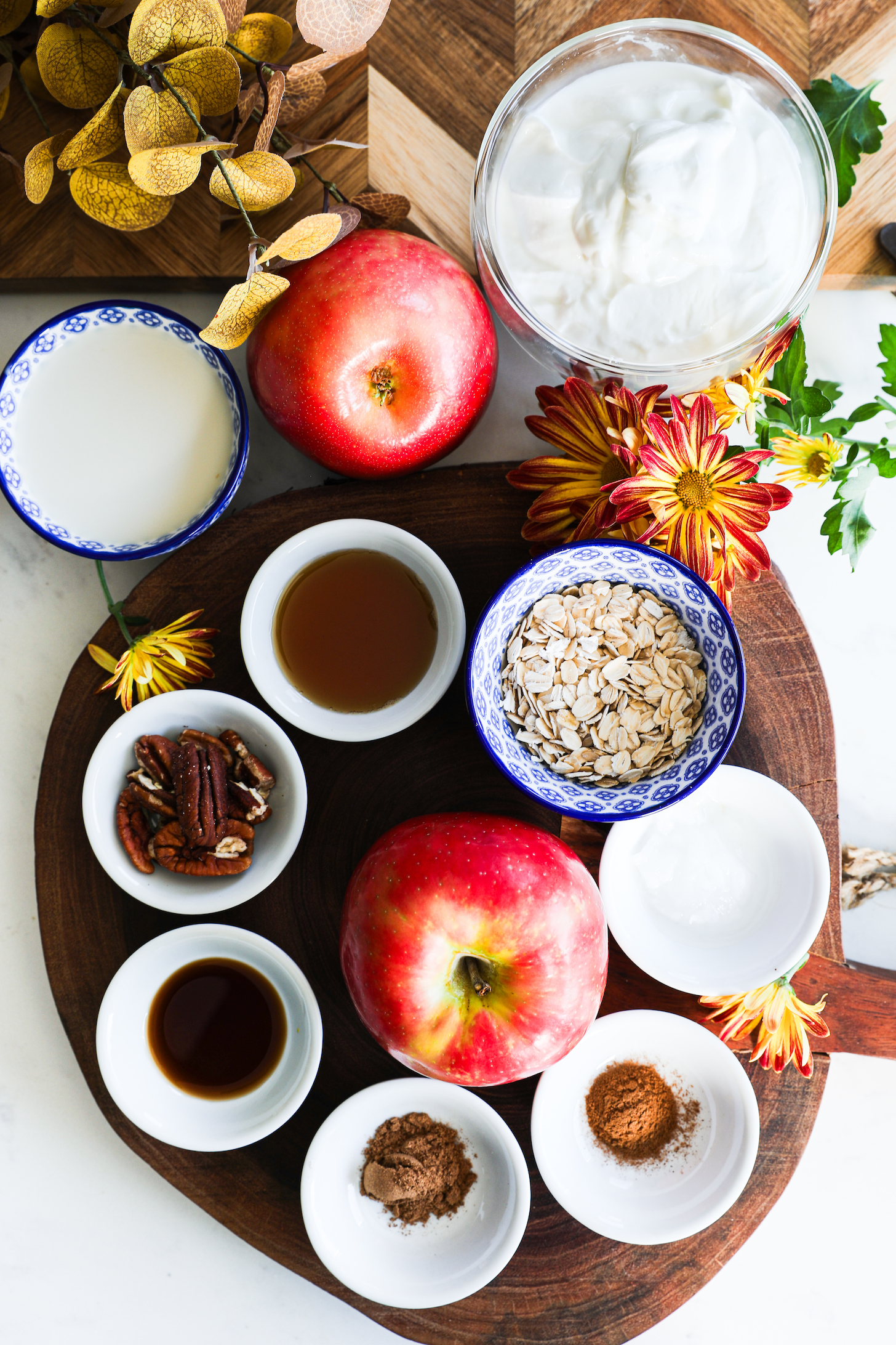 A collection of food ingredients like apples, yogurt, oats, sices and pecans.