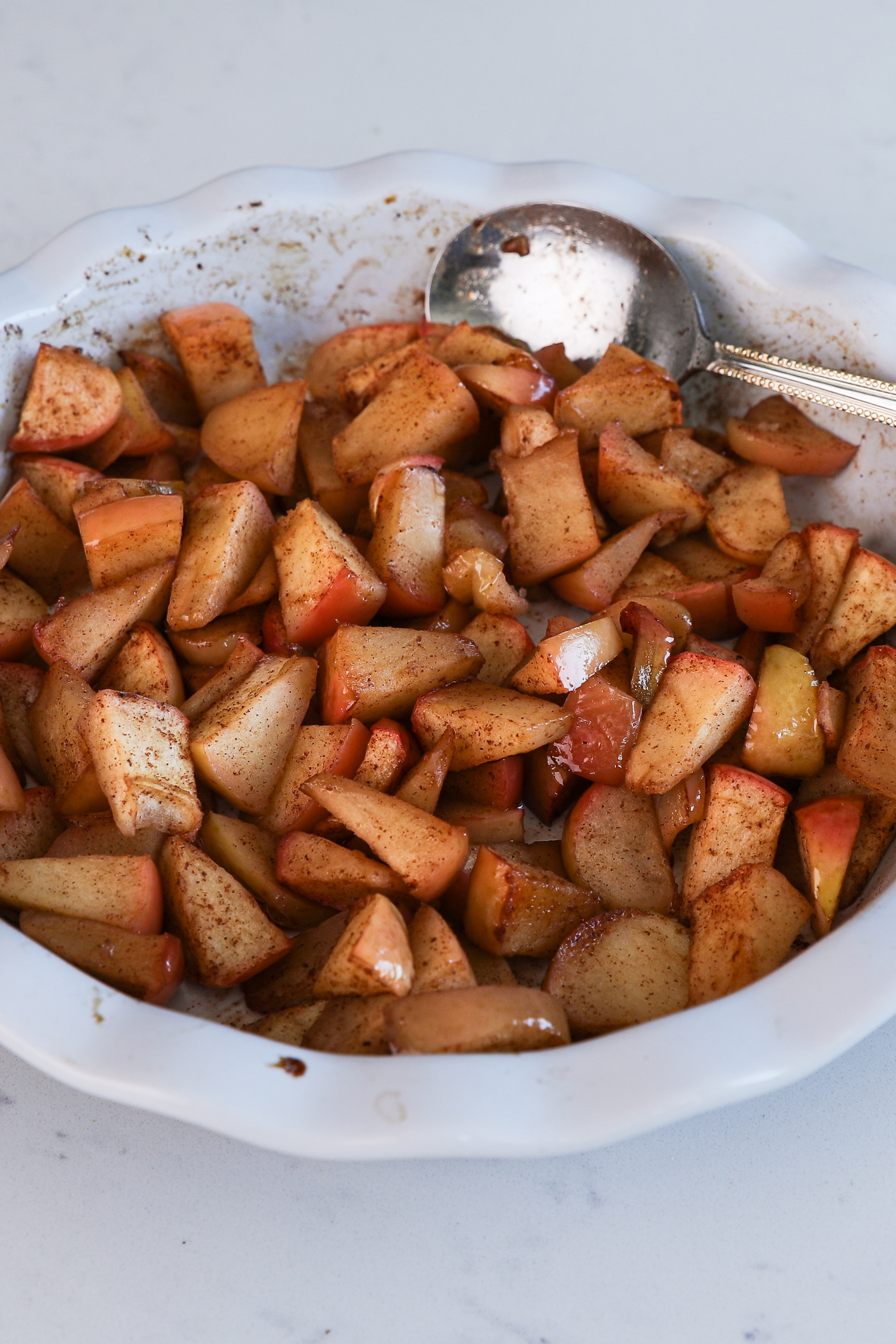 Oven dish with spice-coated baked apple slices and a spoon.