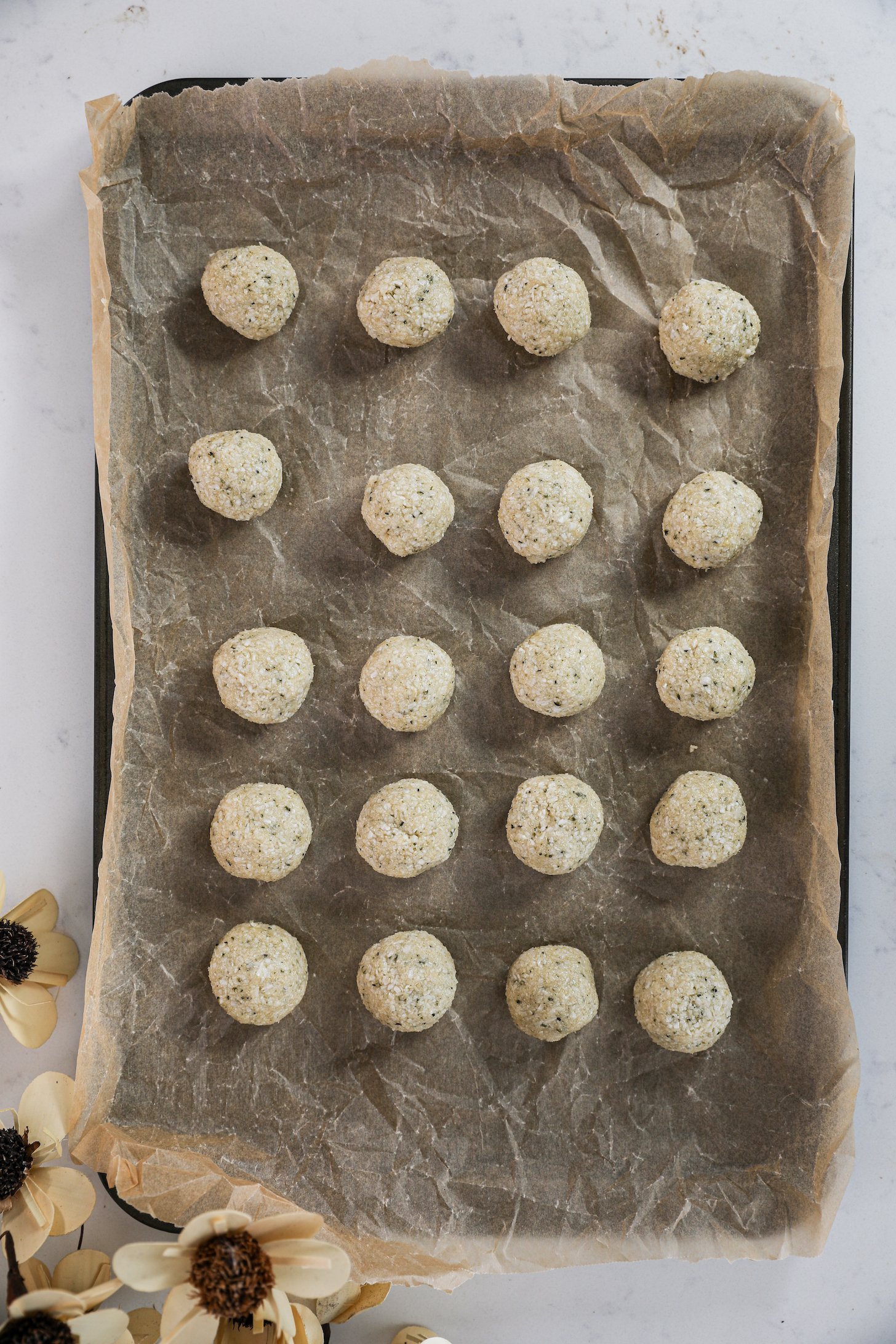 Twenty beige-coloured coconut balls neatly arranged on a lined baking sheet.