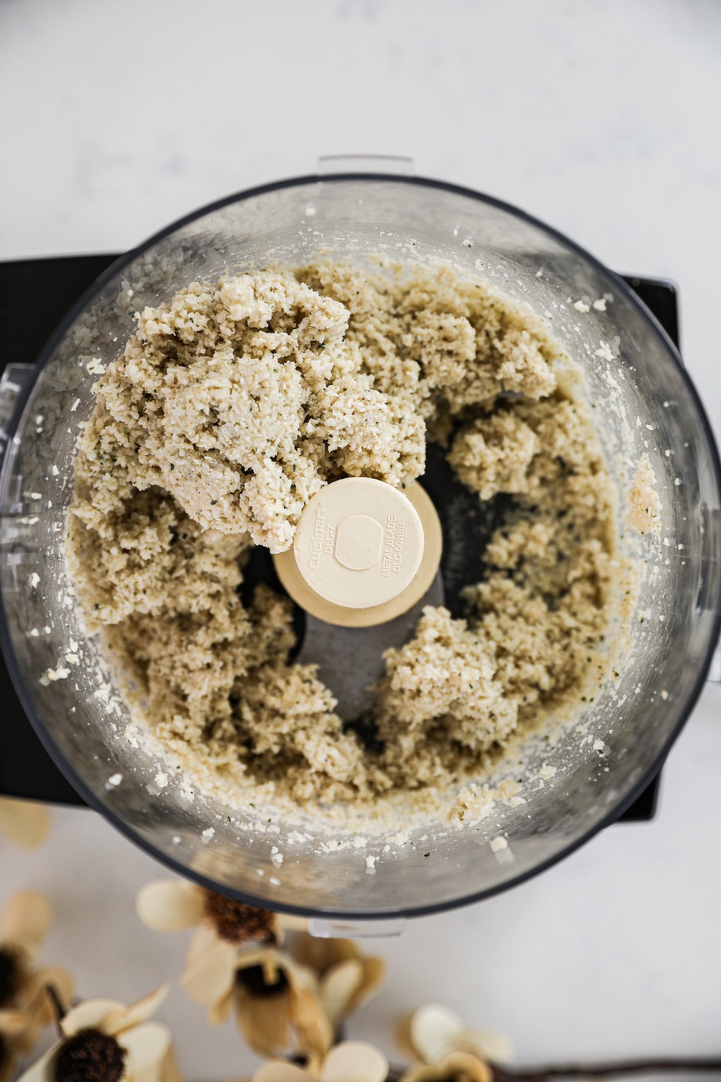 An overhead view of a food processor with finely processed coconut and seeds.