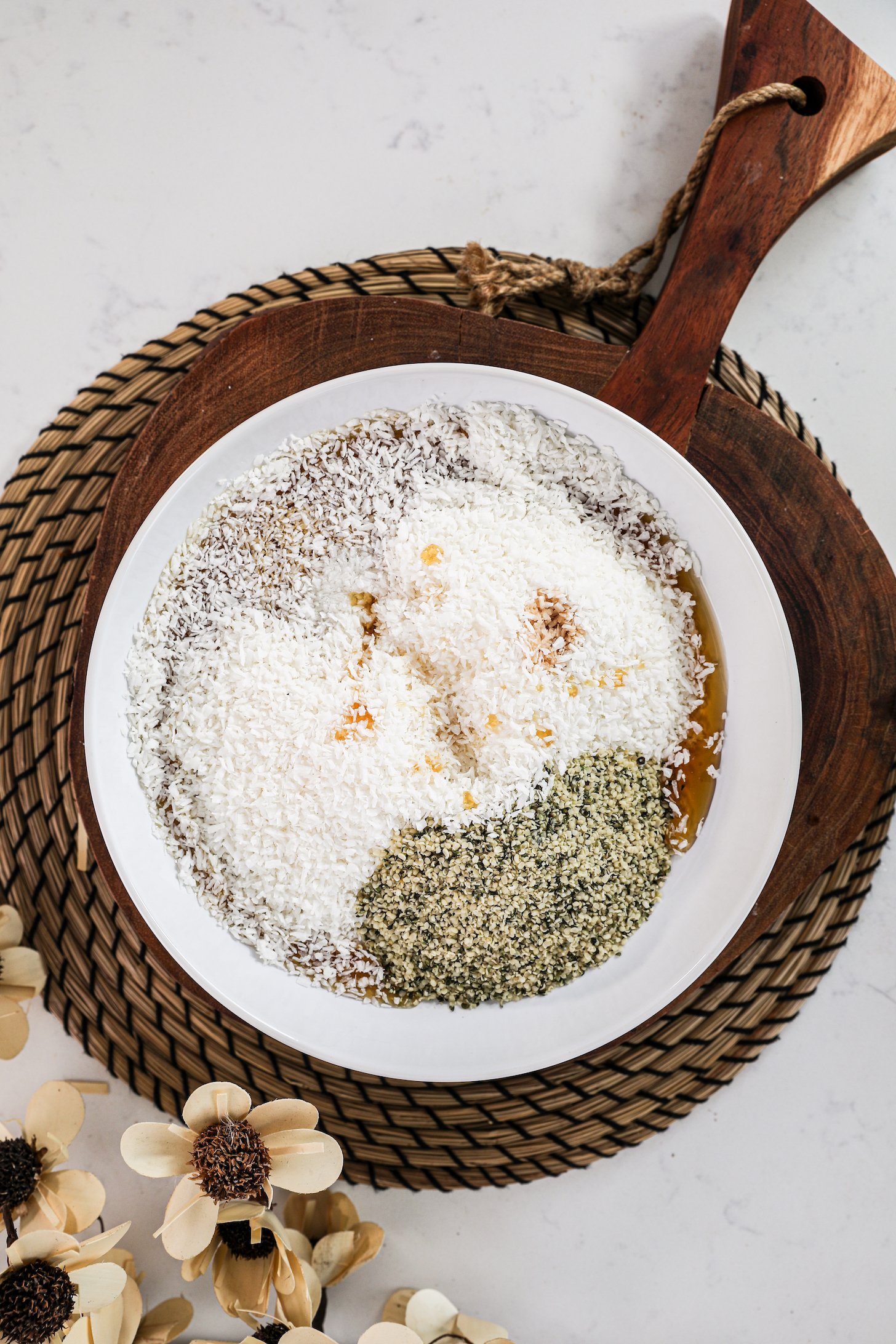 A bowl containing shredded coconut, hemp seeds, vanilla and maple syrup.