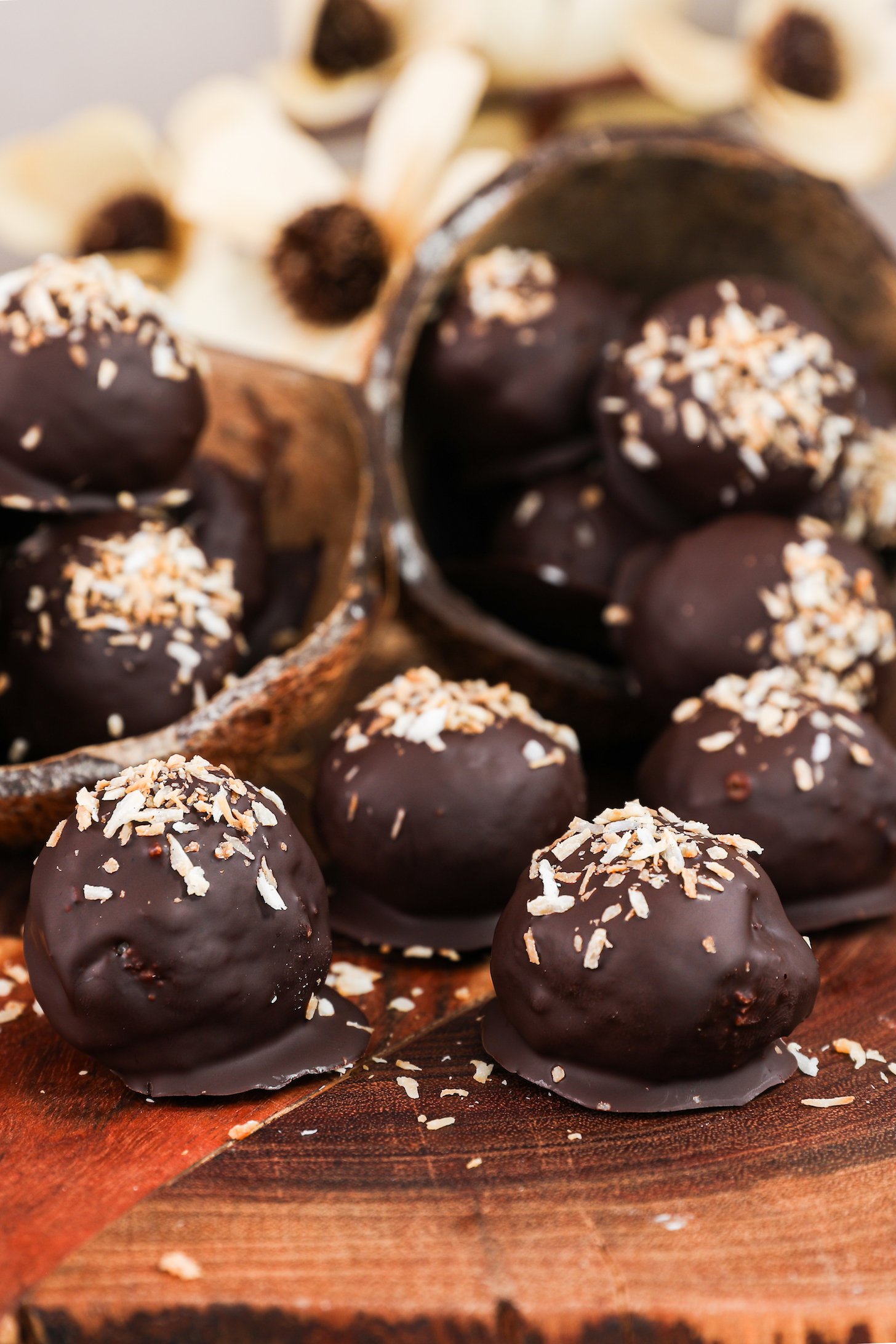 Close up image of chocolate-covered balls with a coconut topping displayed in coconut shells and sitting on a wooden board.