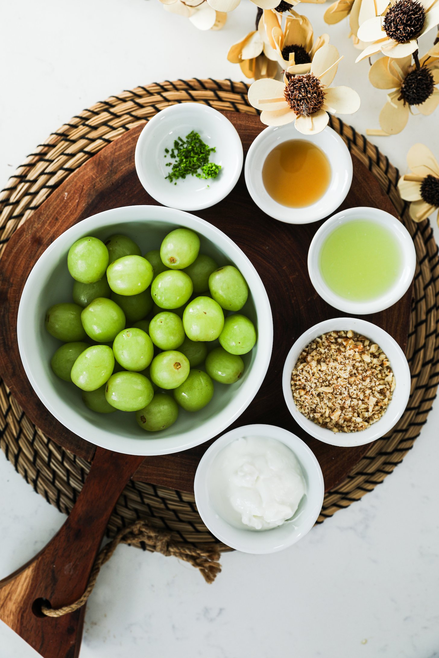 A collection of ingredients, including grapes, nuts, yogurt, maple syrup, lime juice and zest and wooden picks, is laid out, with a nearby sheet pan for assembly.