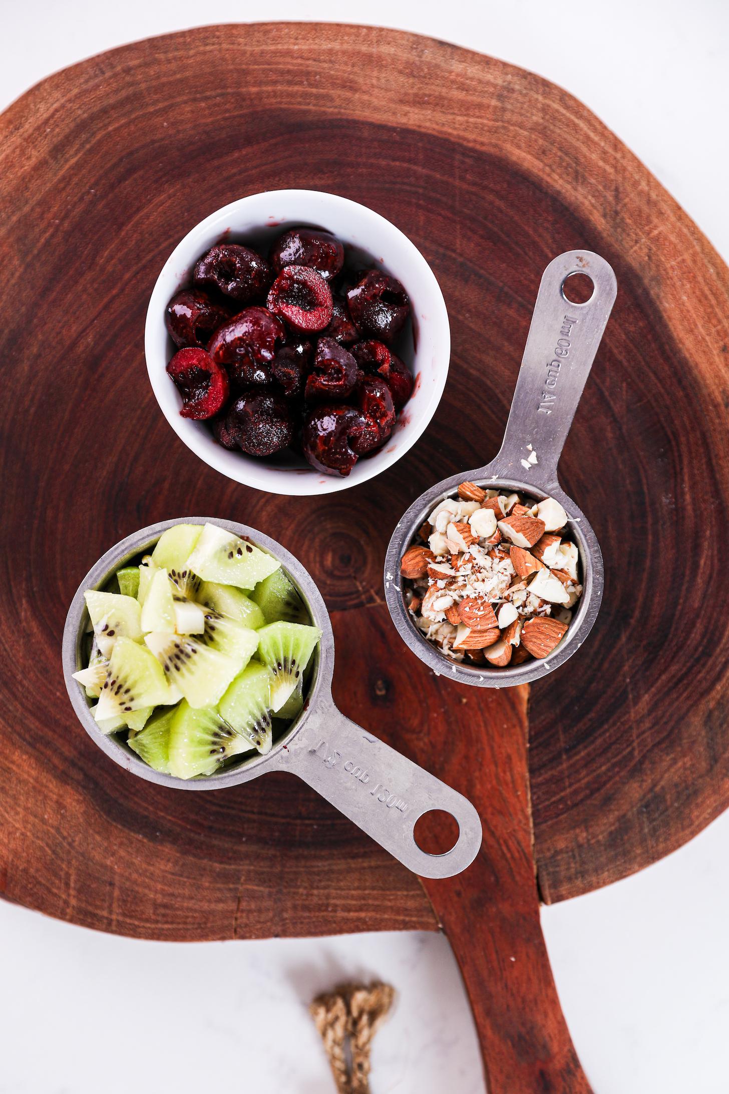 Ramekin and measuring cups brimming with diced cherries, kiwi, and almonds.