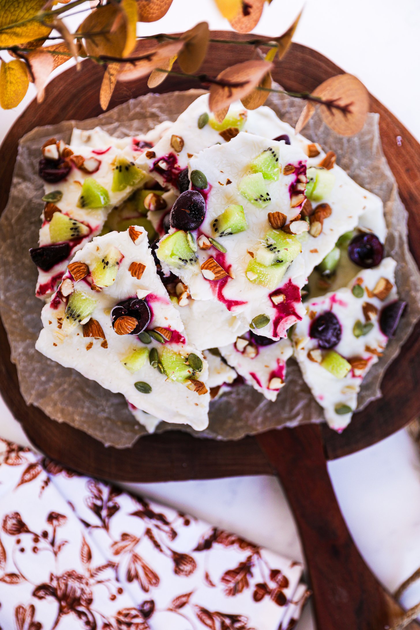 Yogurt bark broken into pieces, adorned with fruit and nuts, displayed on a wooden serving board.