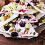 Perspective image of a generous stack of frozen yogurt bark, topped with an assortment of fruits and nuts.