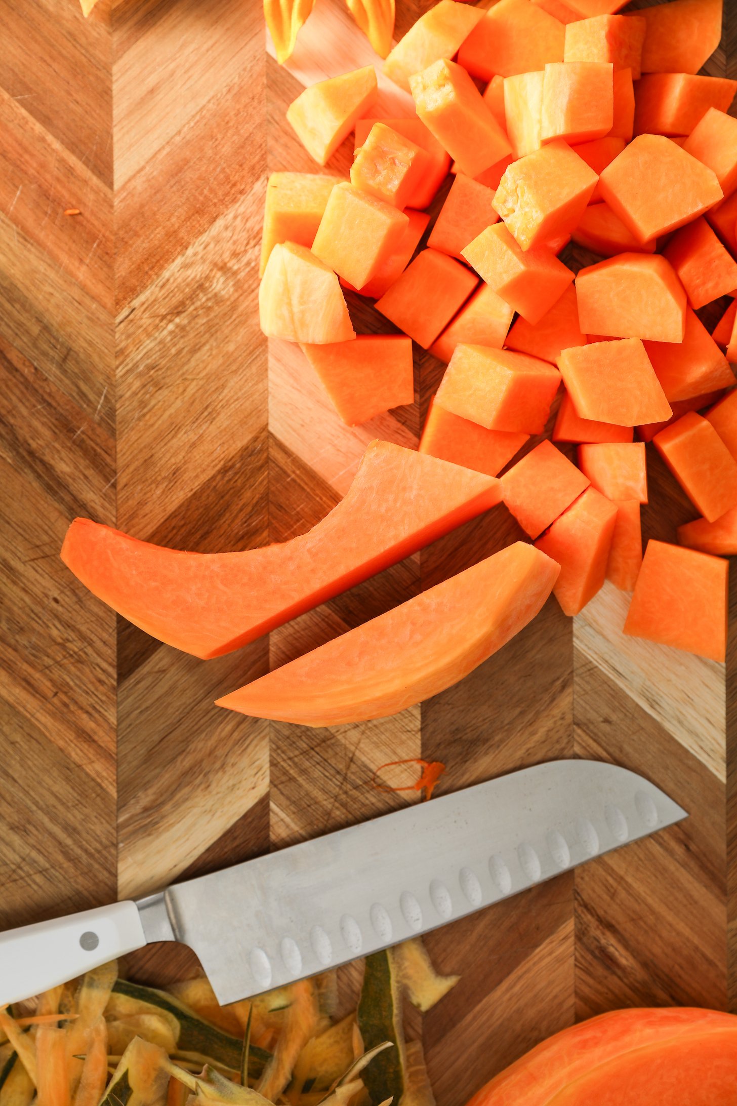 Two pumpkin sticks surrounded by chunks of pumpkin on a wooden board with a knife closeby.