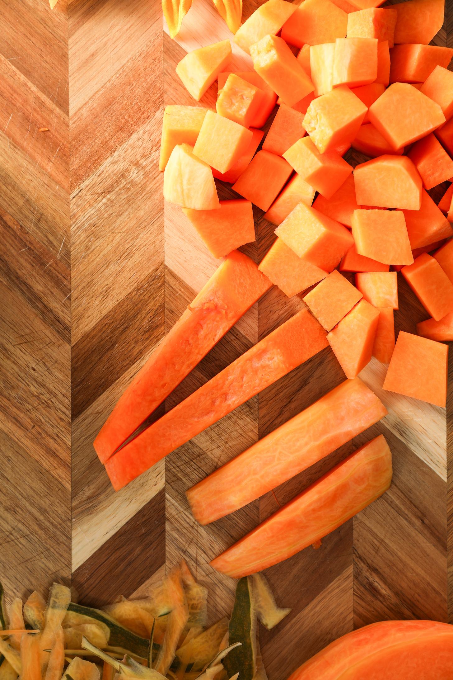 Four pumpkin sticks surrounded by chunks of pumpkin on a wooden board.