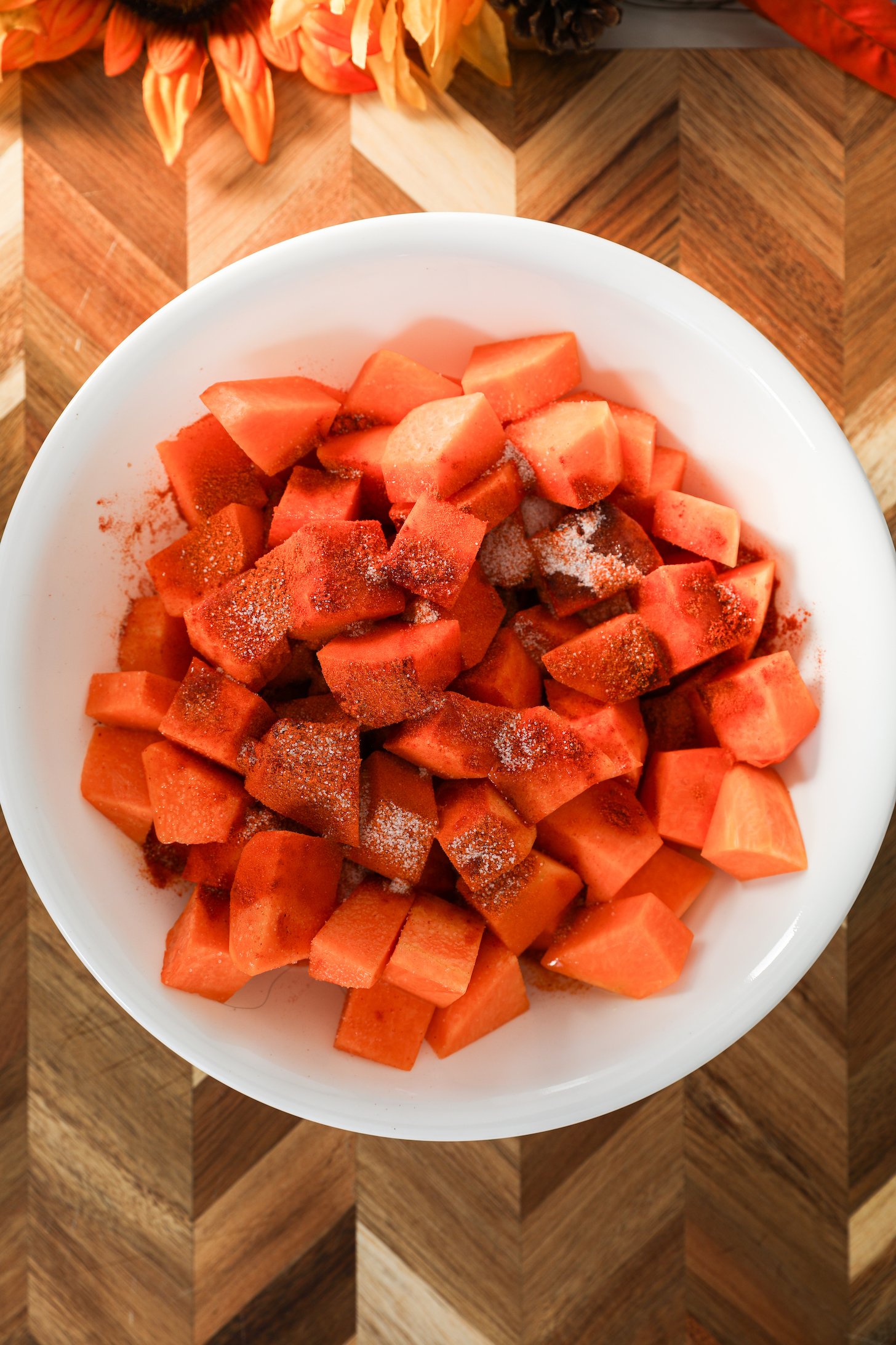 A large bowl of pumpkin chunks topped with powdered spices, surrounded on a wooden board.