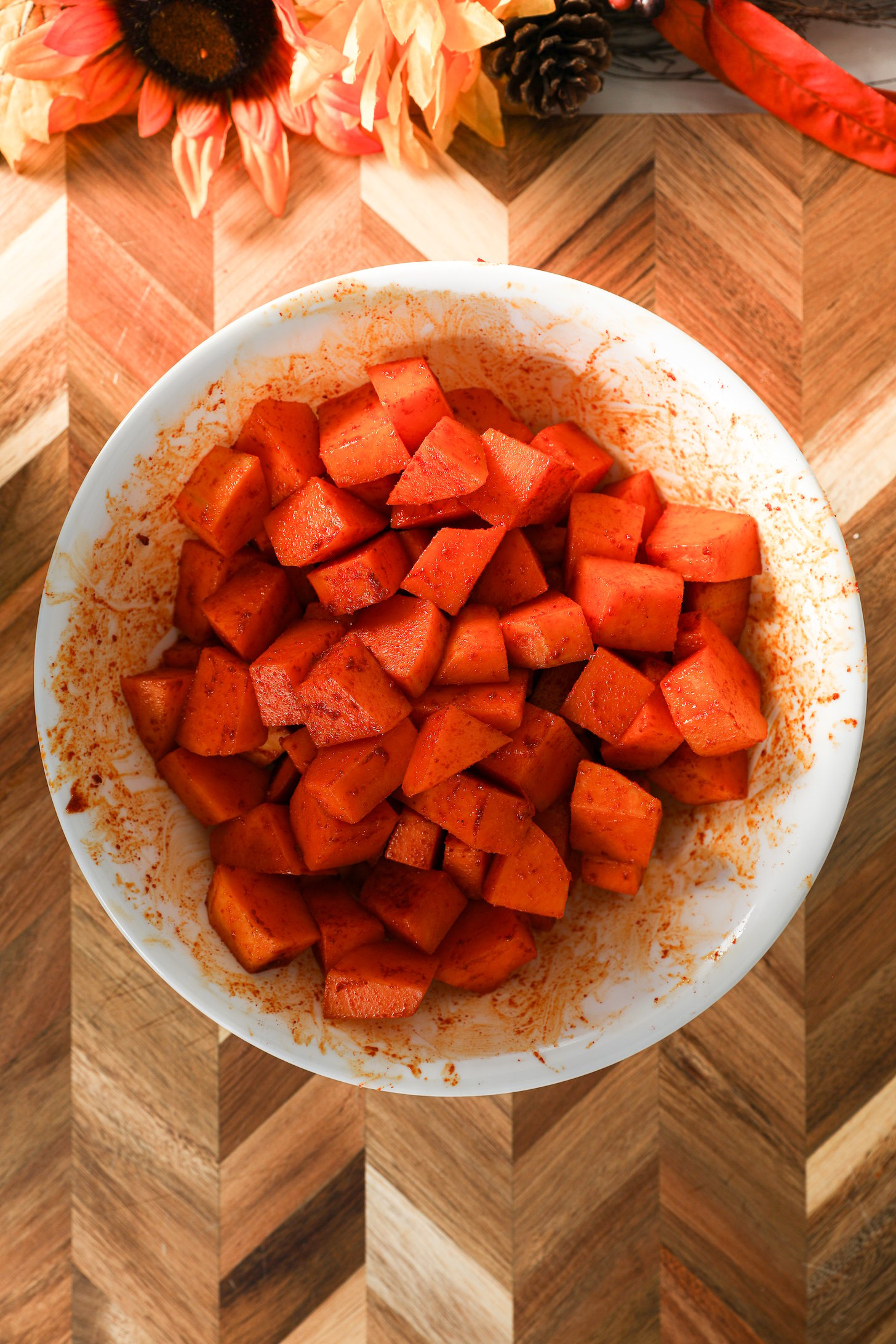 A large bowl of spice-coated pumpkin chunks, surrounded on a wooden board.