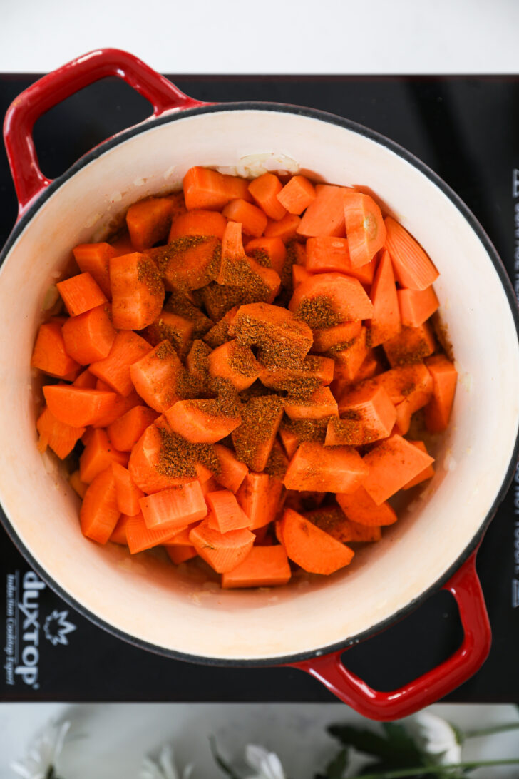 A cooking pot filled with diced carrots and sweet potato chunks sprinkled with powdered spices.