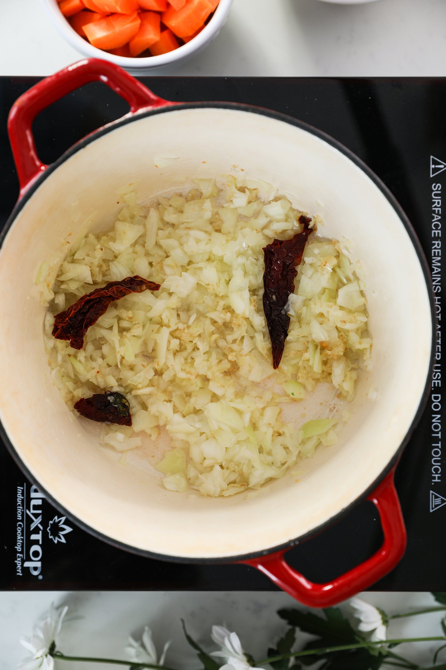 A cooking pot on a mobile cooktop containing sautéed chopped onion and dried red chillies.