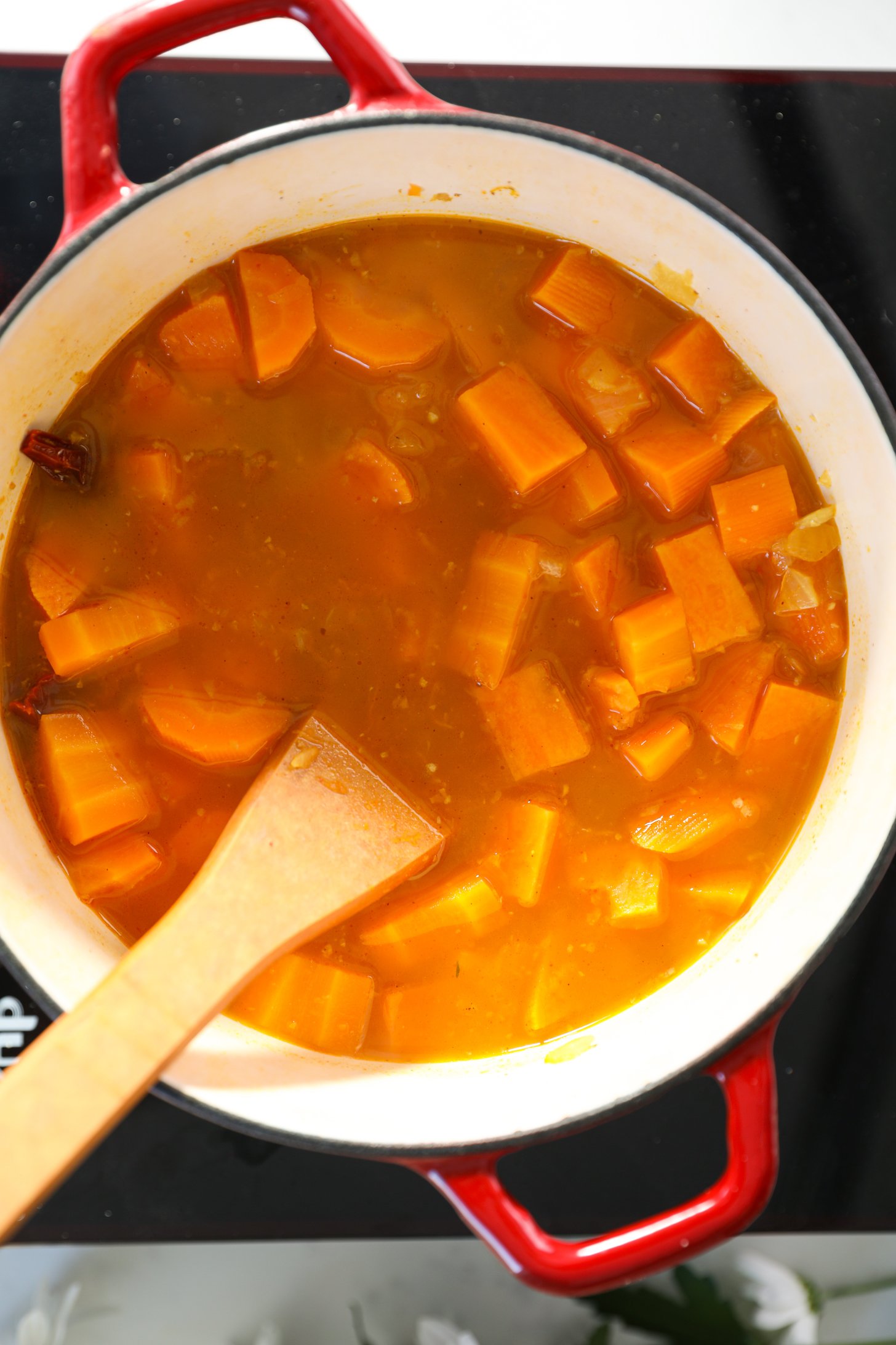 A cooking pot filled with diced sweet potato and carrot chunks in stock, with a wooden spoon submerged in it.