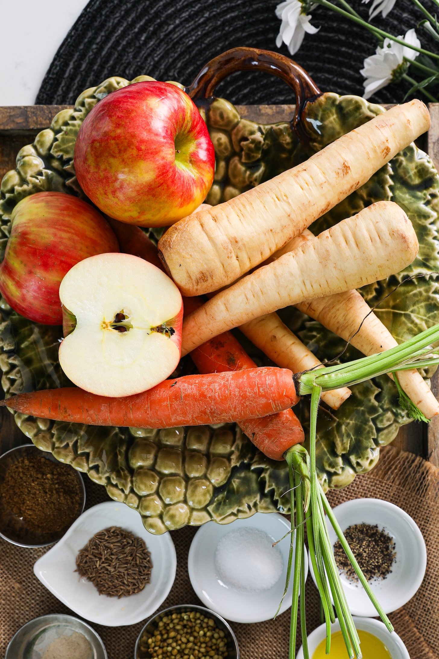 Overhead view of whole parsnips, carrots and apples alongside ramekins of spices.