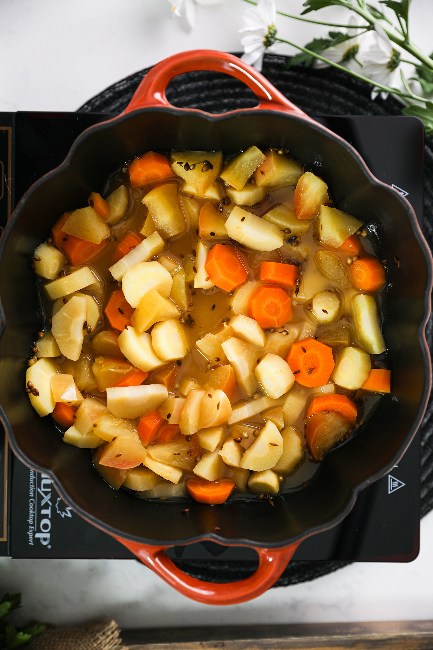 Overhead view of diced parsnips, apple, and carrots in stock inside a cooking pot.
