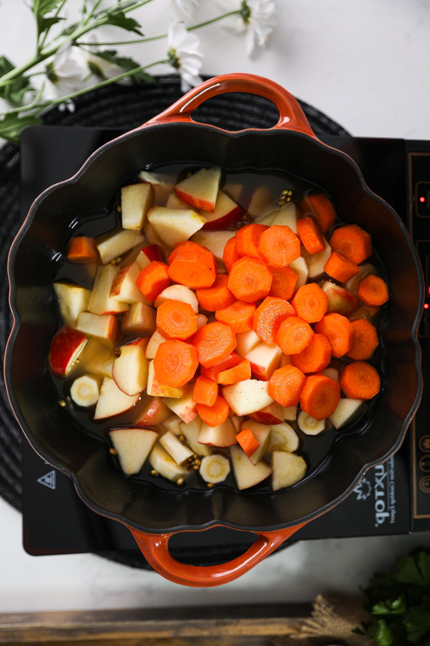 Overhead view of diced carrots, apple, and parsnips in stock inside a cooking pot.