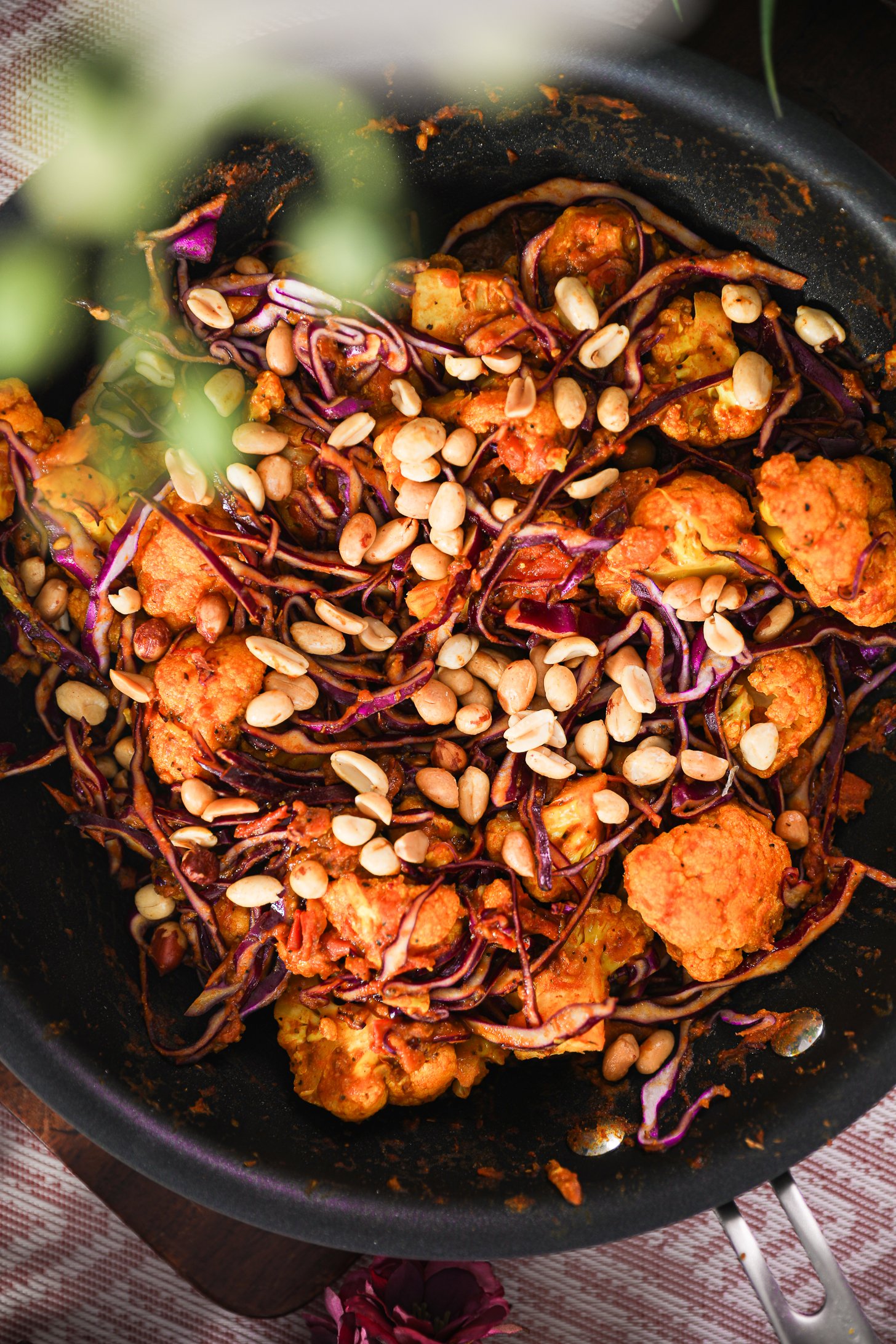 Close-up image of pan of stir fired cabbage and cauliflower topped with peanuts.