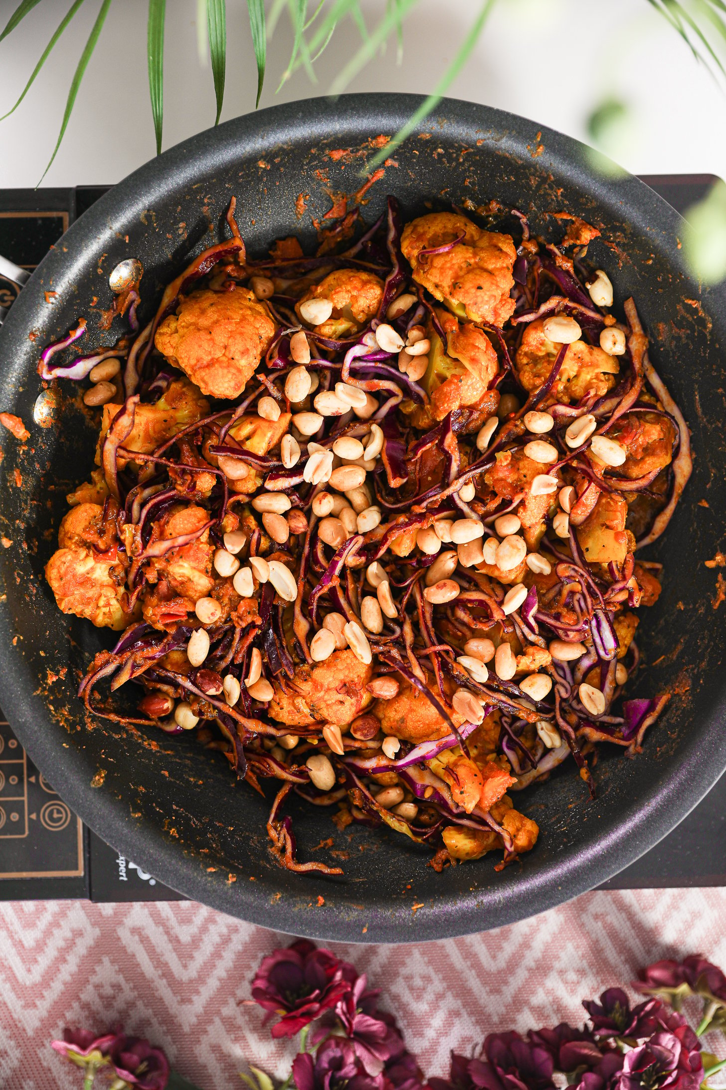A pan of stir fried cabbage and cauliflower topped with peanuts on a mobile worktop.