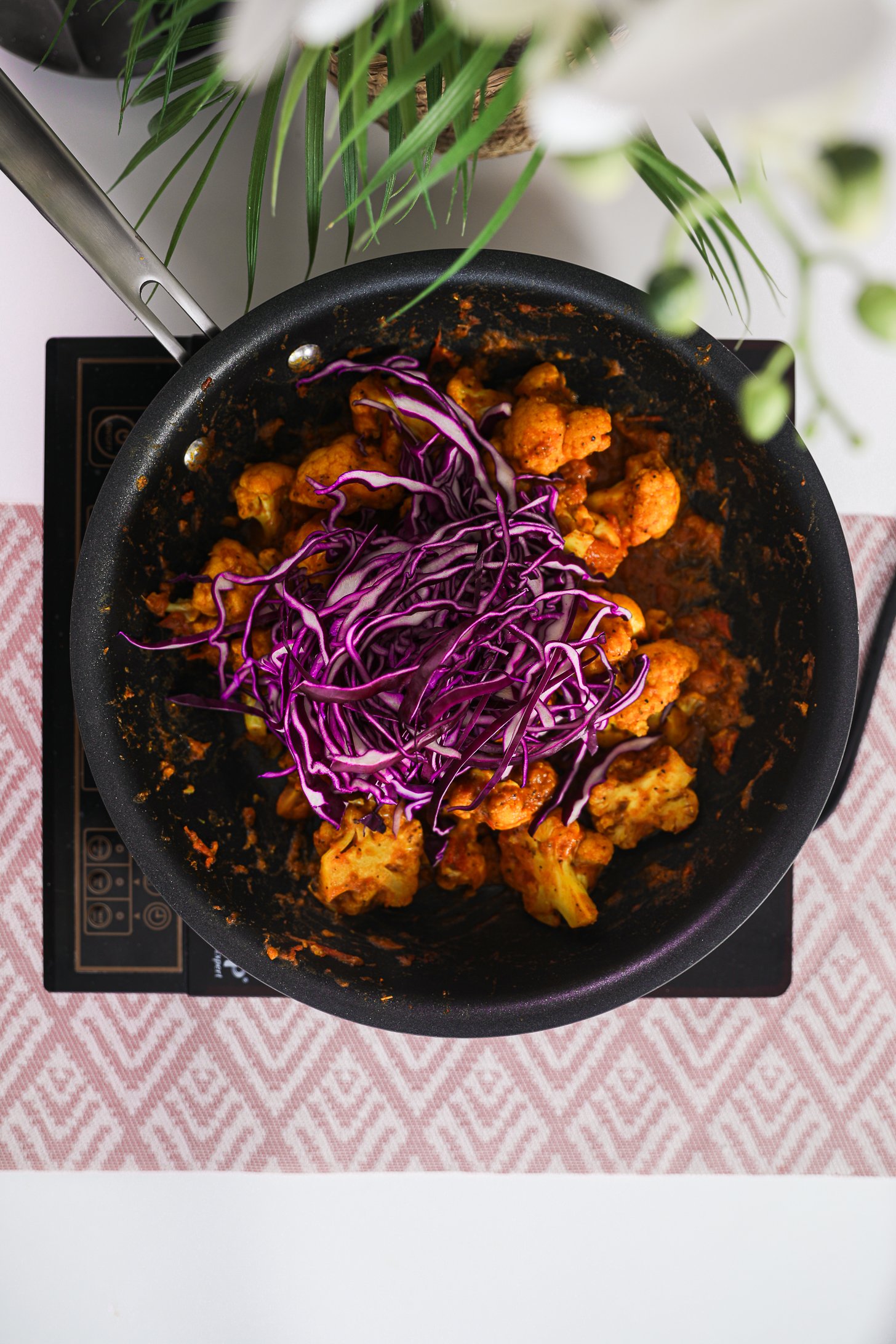 A pan of stir fried cauliflower topped with vibrant purple cabbage threads on a mobile worktop.