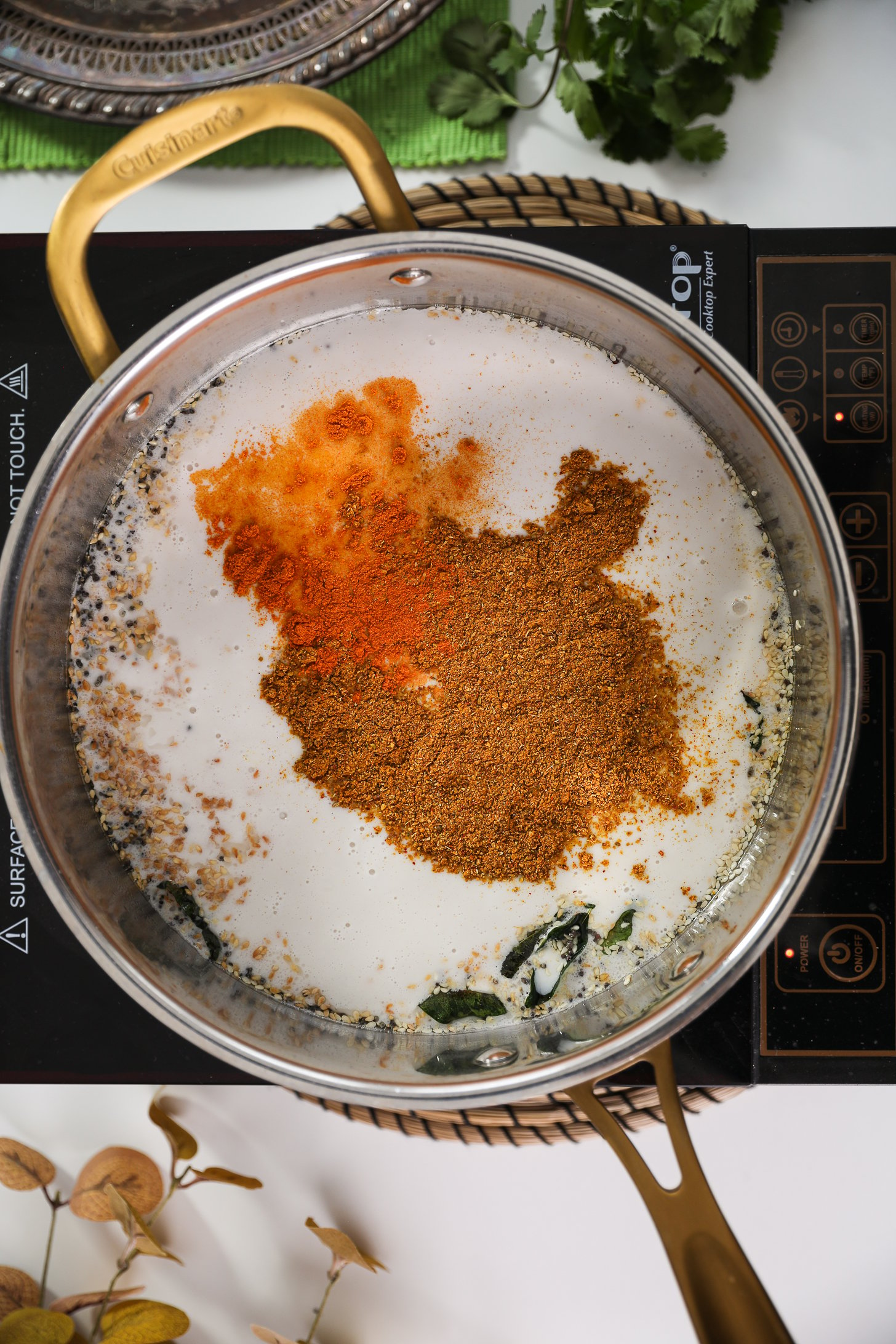 A mobile cooktop displaying a pan filled with coconut milk and topped with a dusting of powdered spices.
