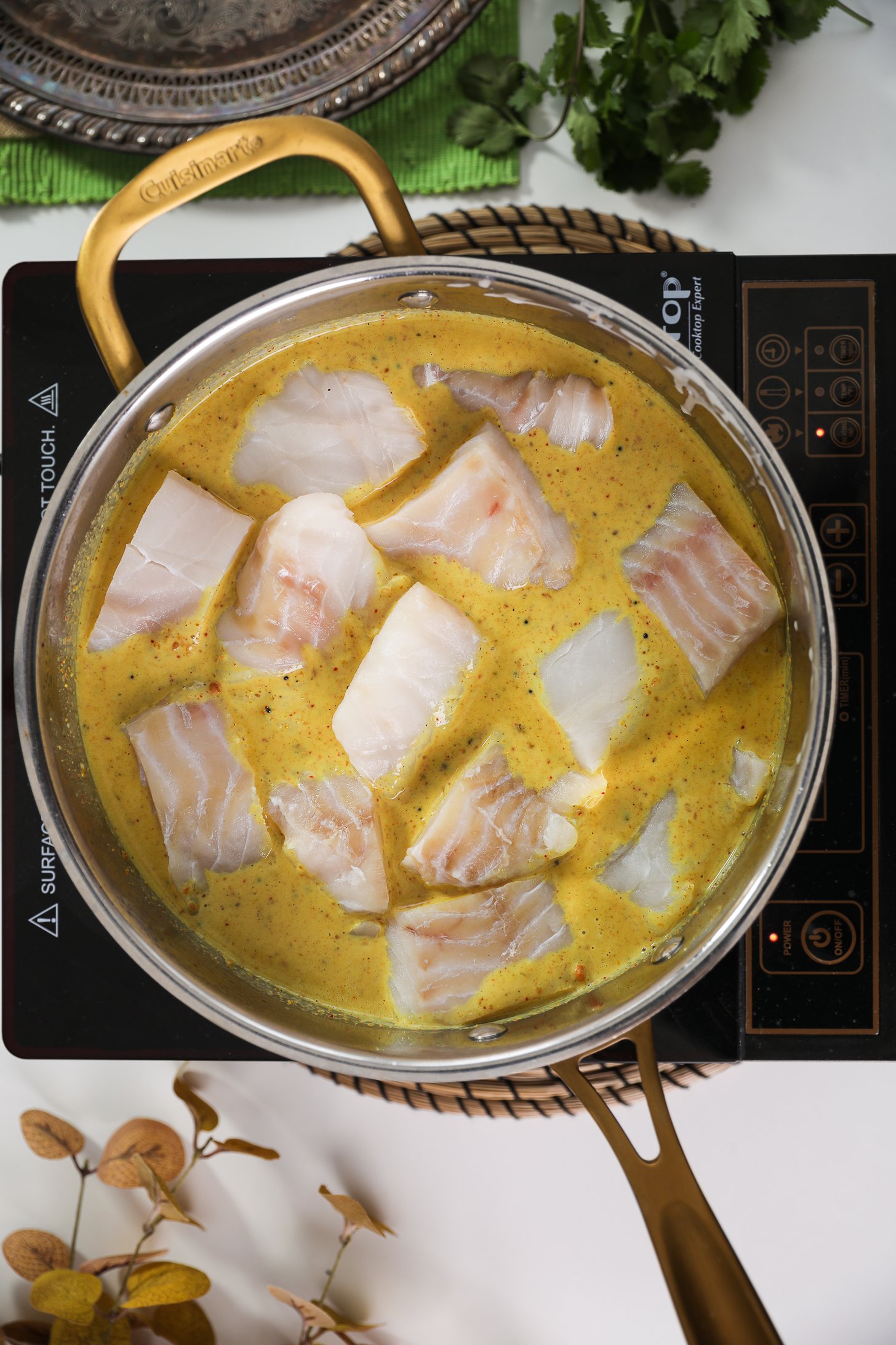 Mobile cooktop showcasing a pan of fish fillets placed in a curry sauce.