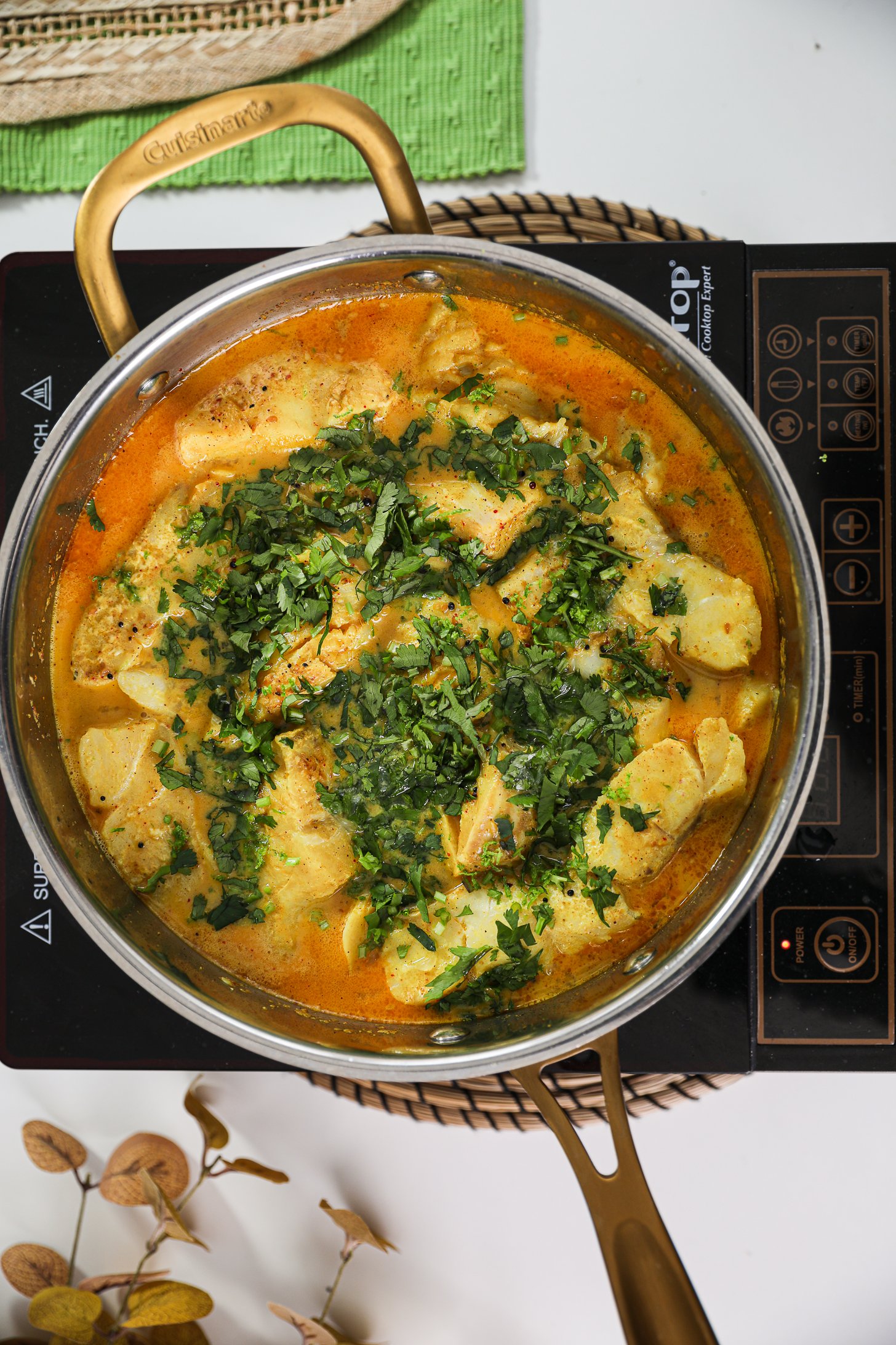 Pan of fish fillets in a curry sauce topped with cilantro placed on a mobile cooktop.