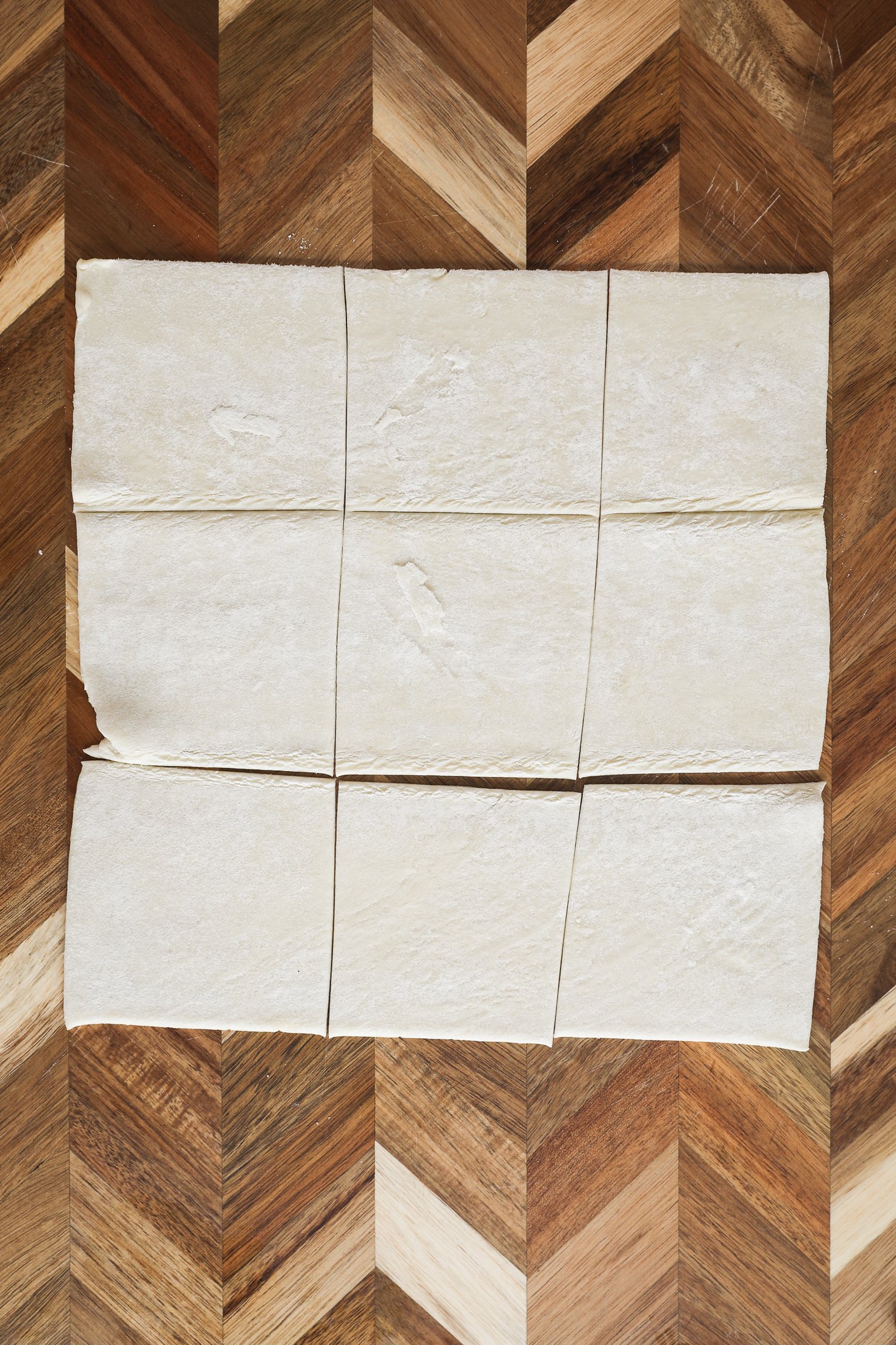 Puff pastry sheet cut into nine squares on a wooden board.