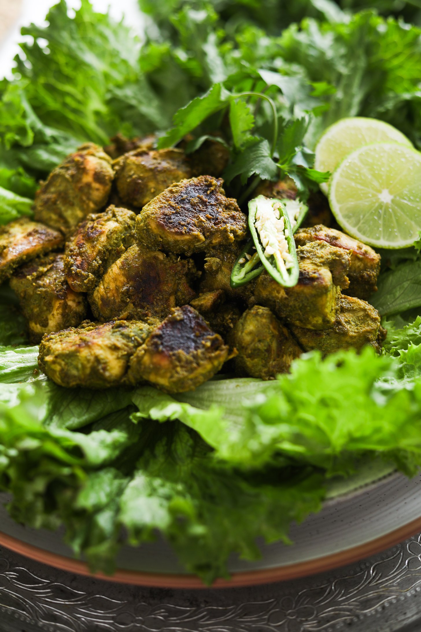 Perspective image of green chicken (Hariyali chicken) breast pieces placed on lettuce leaves garnished with chilli and lime.