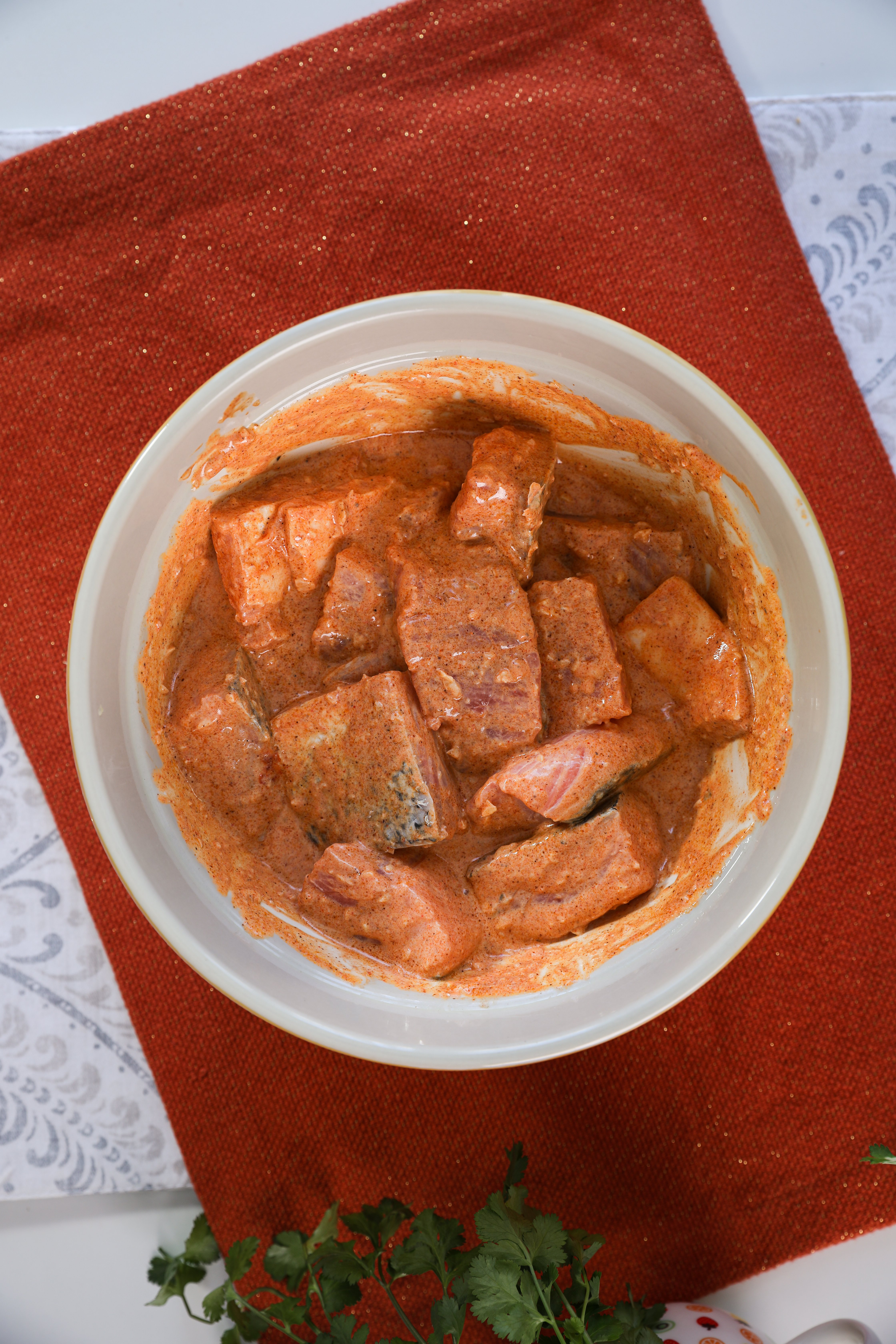 A bowl containing marinated salmon pieces sits on an orange mat.