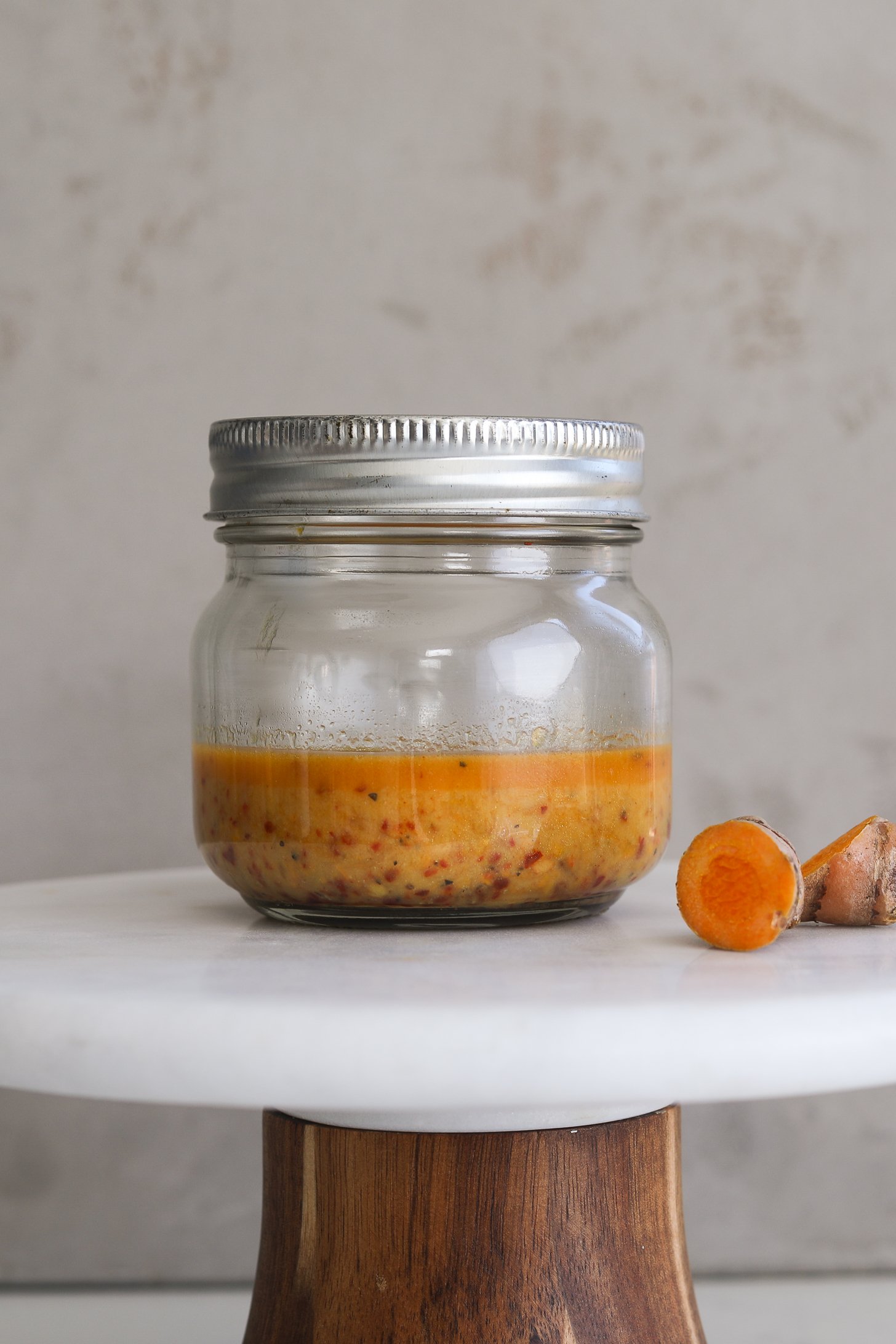 Close up image of a small mason jar of orange dressing on a white stand.