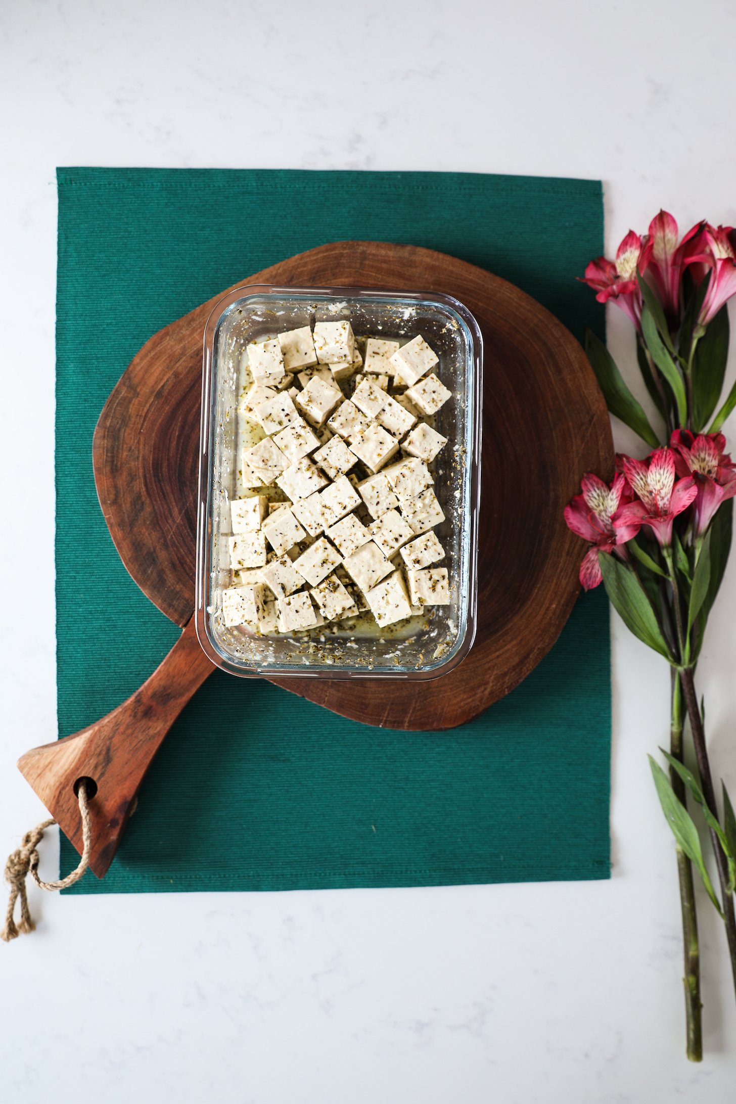 Top view of a container with marinated cubes of tofu with flower stems nearby.