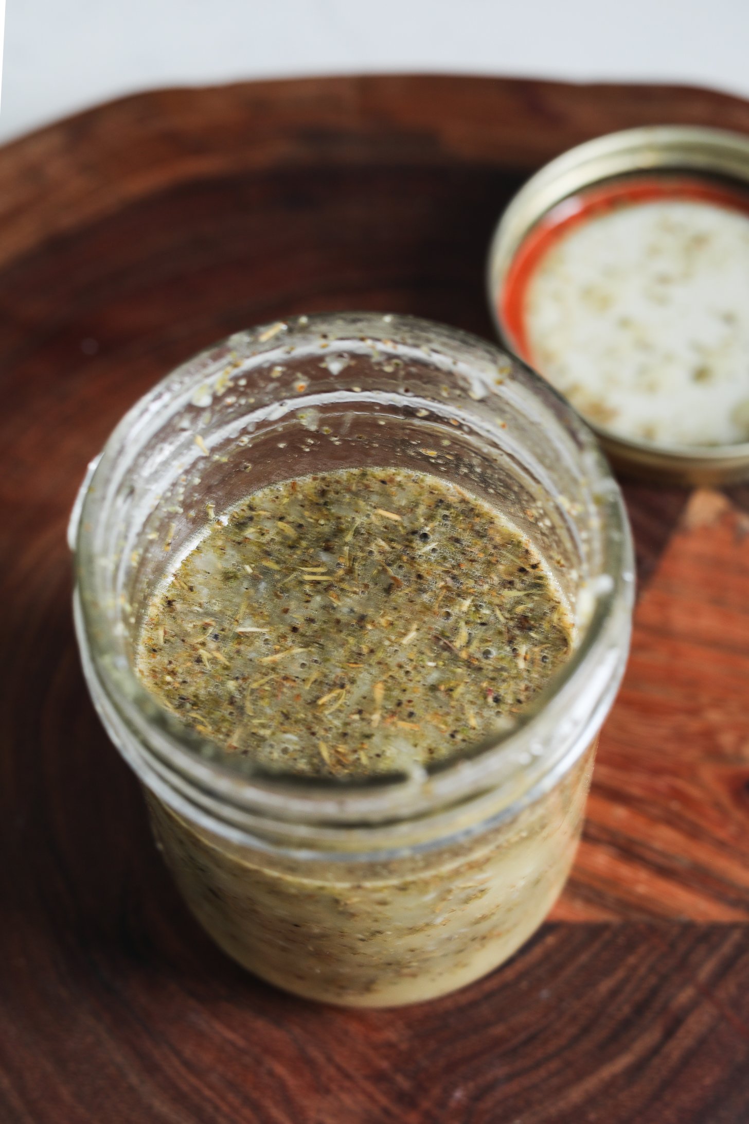 Perspective view of a mason jar filled with dressing adorned with floating dried herbs.