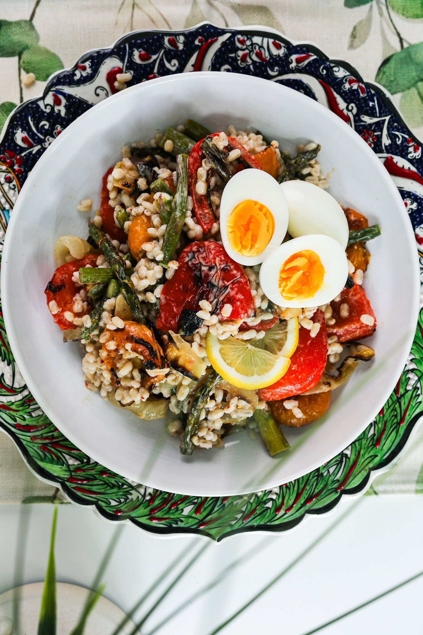 Top view image of a bowl of barley salad with mixed grilled veggie topped with boiled egg halves.
