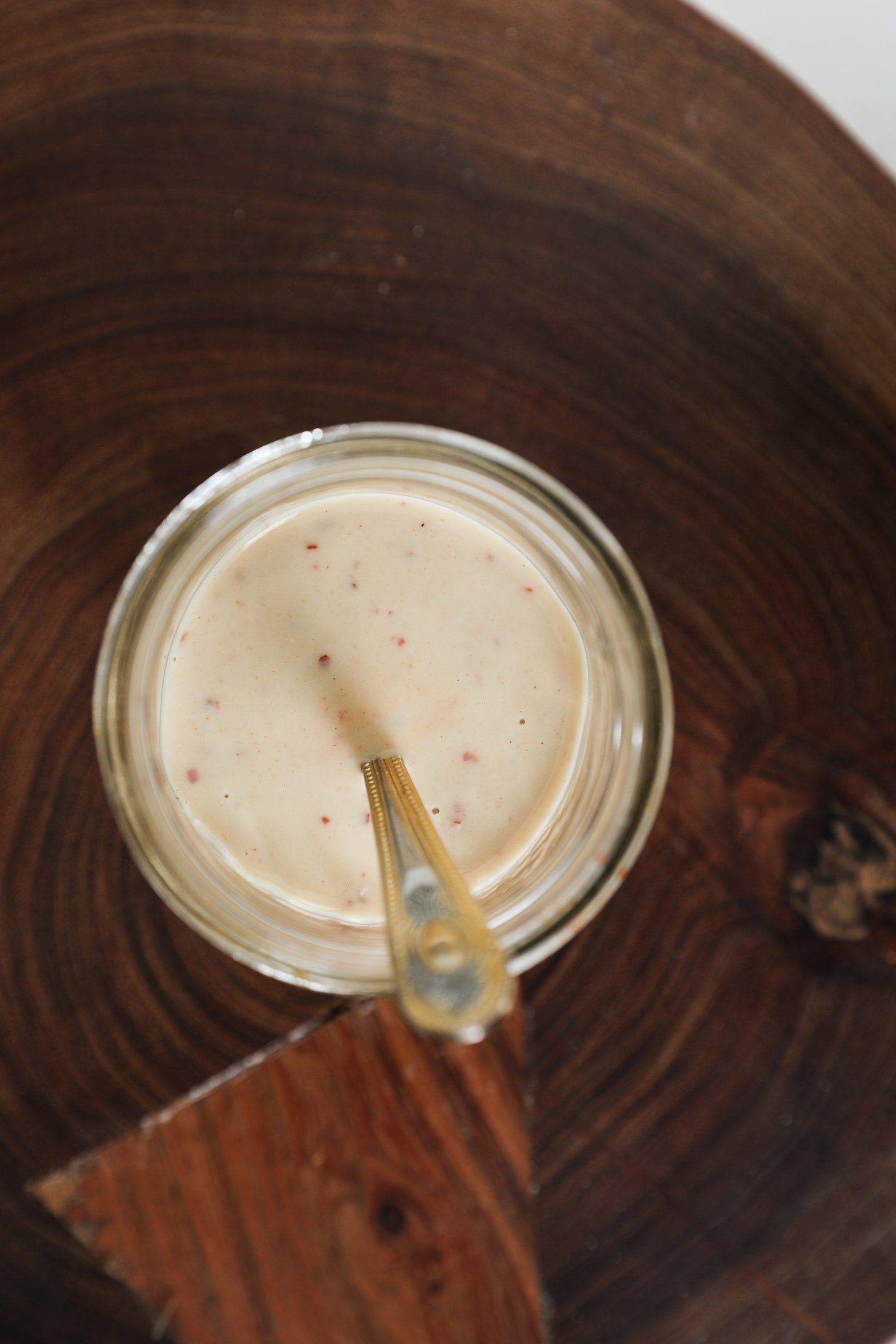 A mason jar holds creamy white salad dressing, with a spoon resting inside.