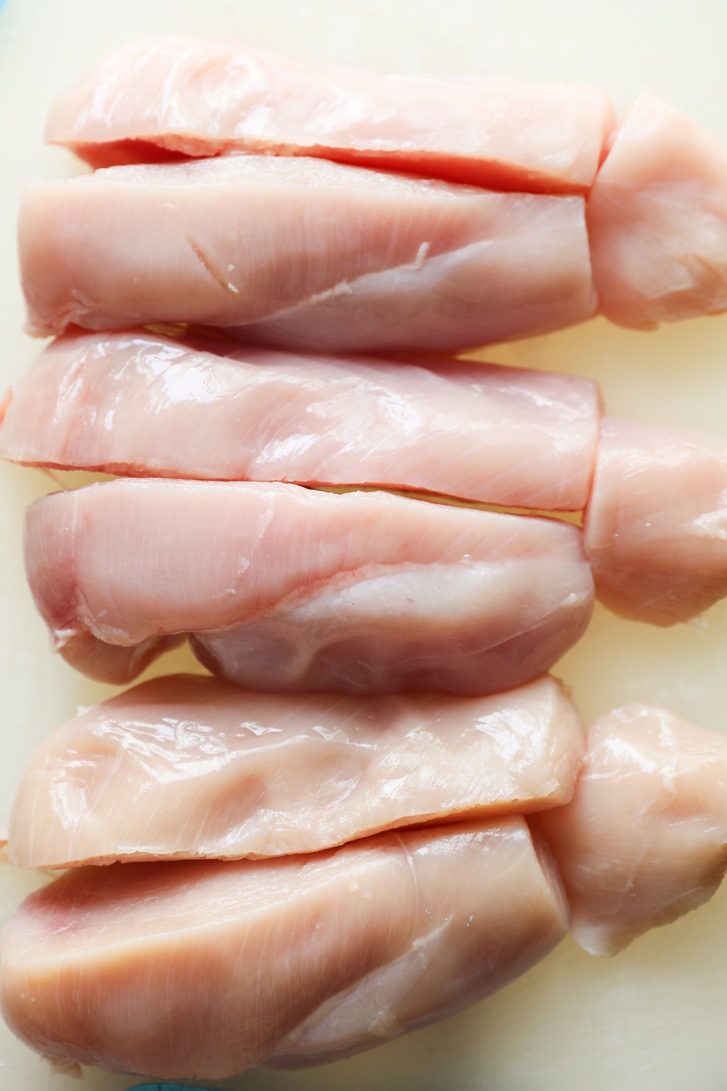 Close up image of chicken breast fillets slit in half with the ends cut off.