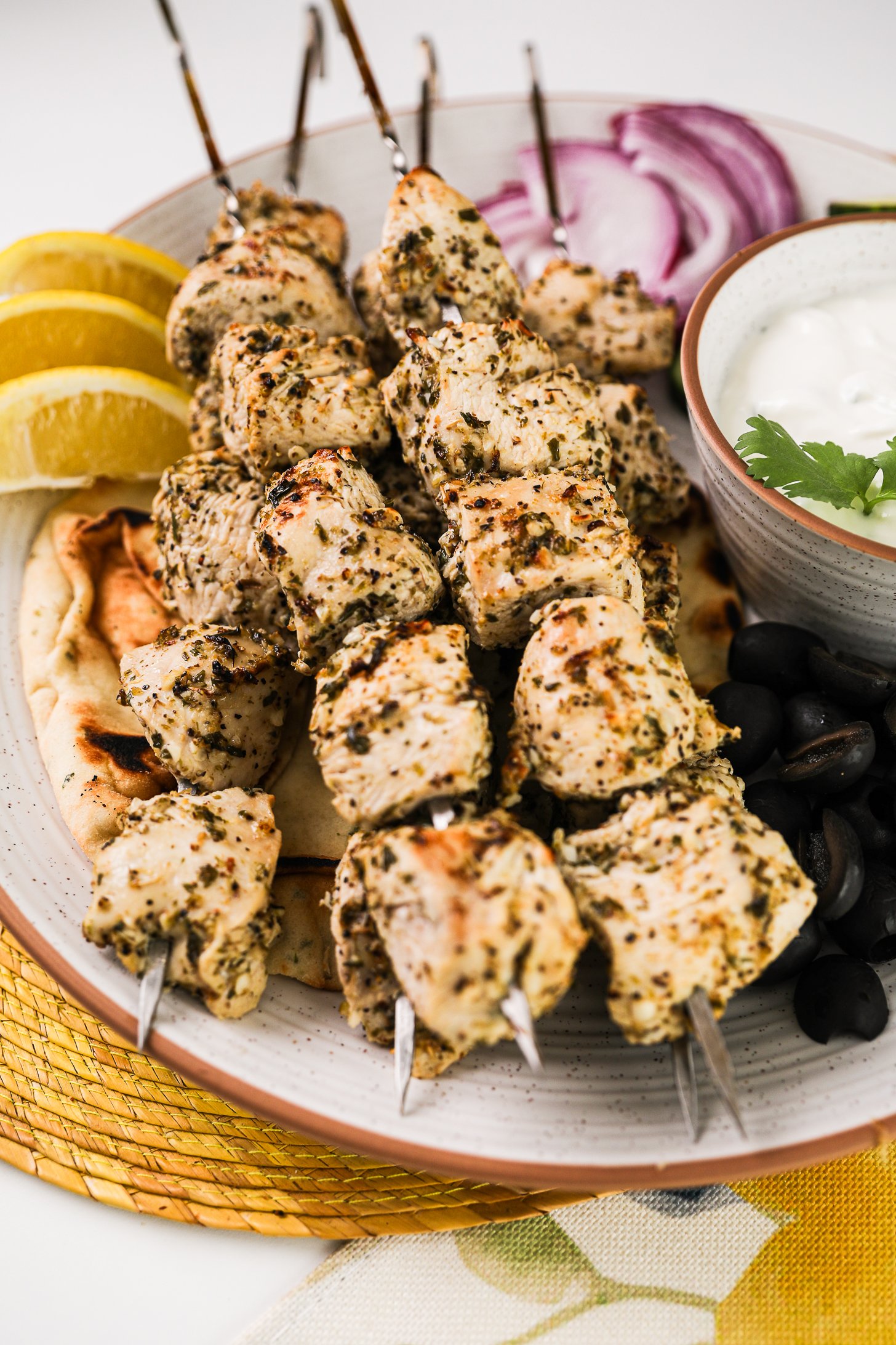 Perspective image of skewers of souvlaki chicken atop a pita with veggies and tzatziki.