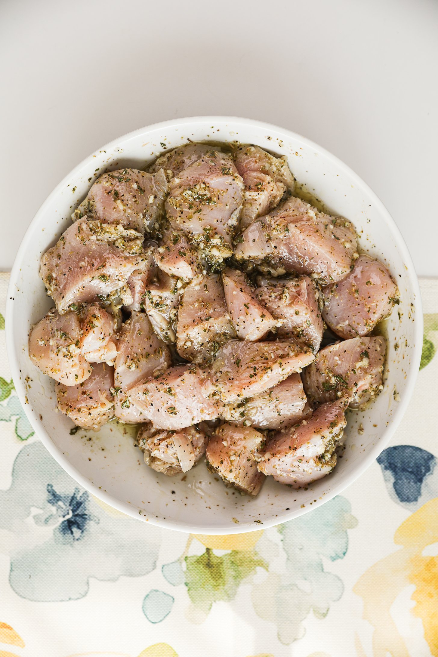 A bowl of marinated raw chicken breast cubes.